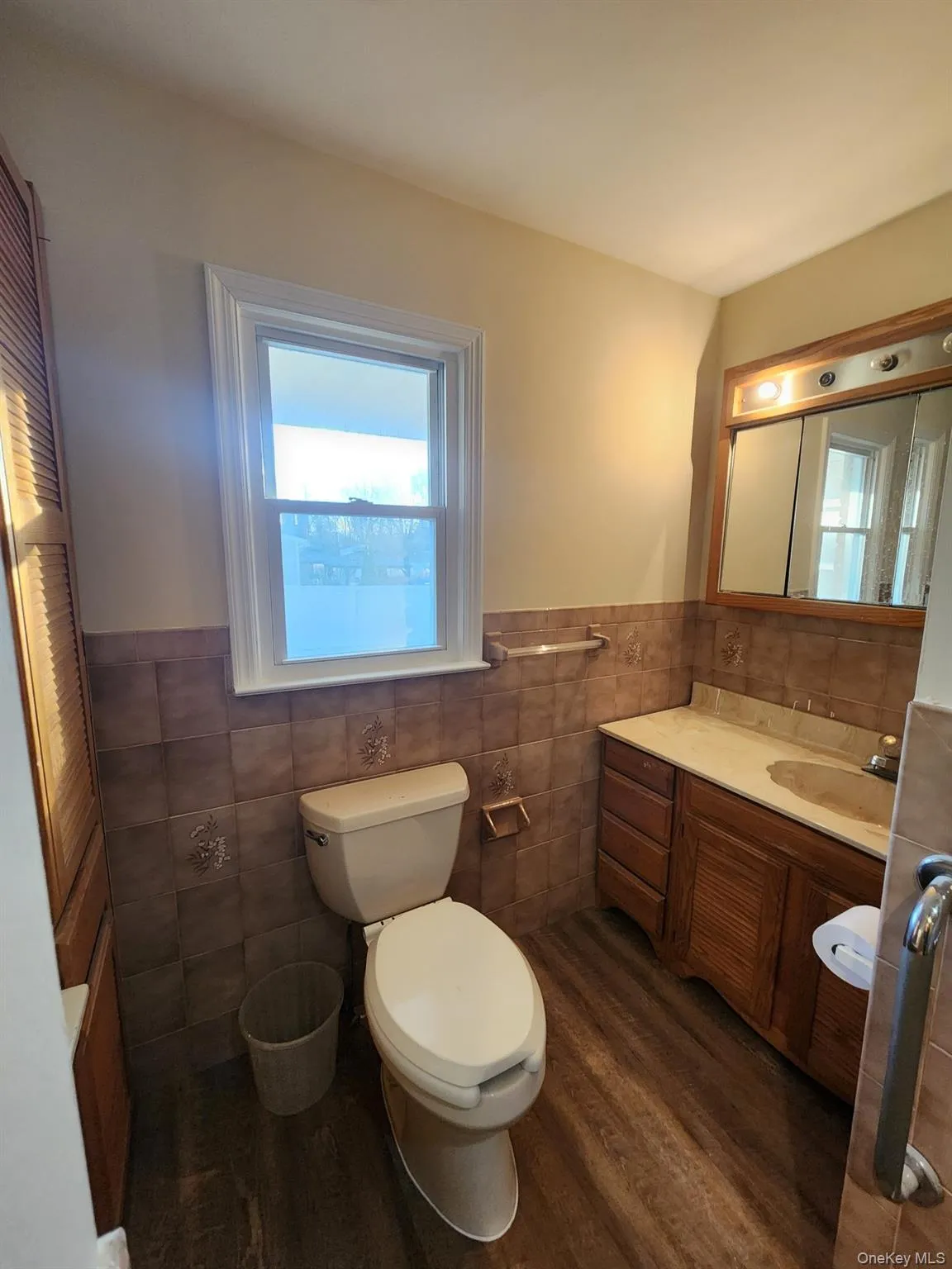 Bathroom featuring vanity, wainscoting, dark wood-type flooring, and tile walls Bathroom featuring vanity, wainscoting, dark wood-type flooring, and tile walls