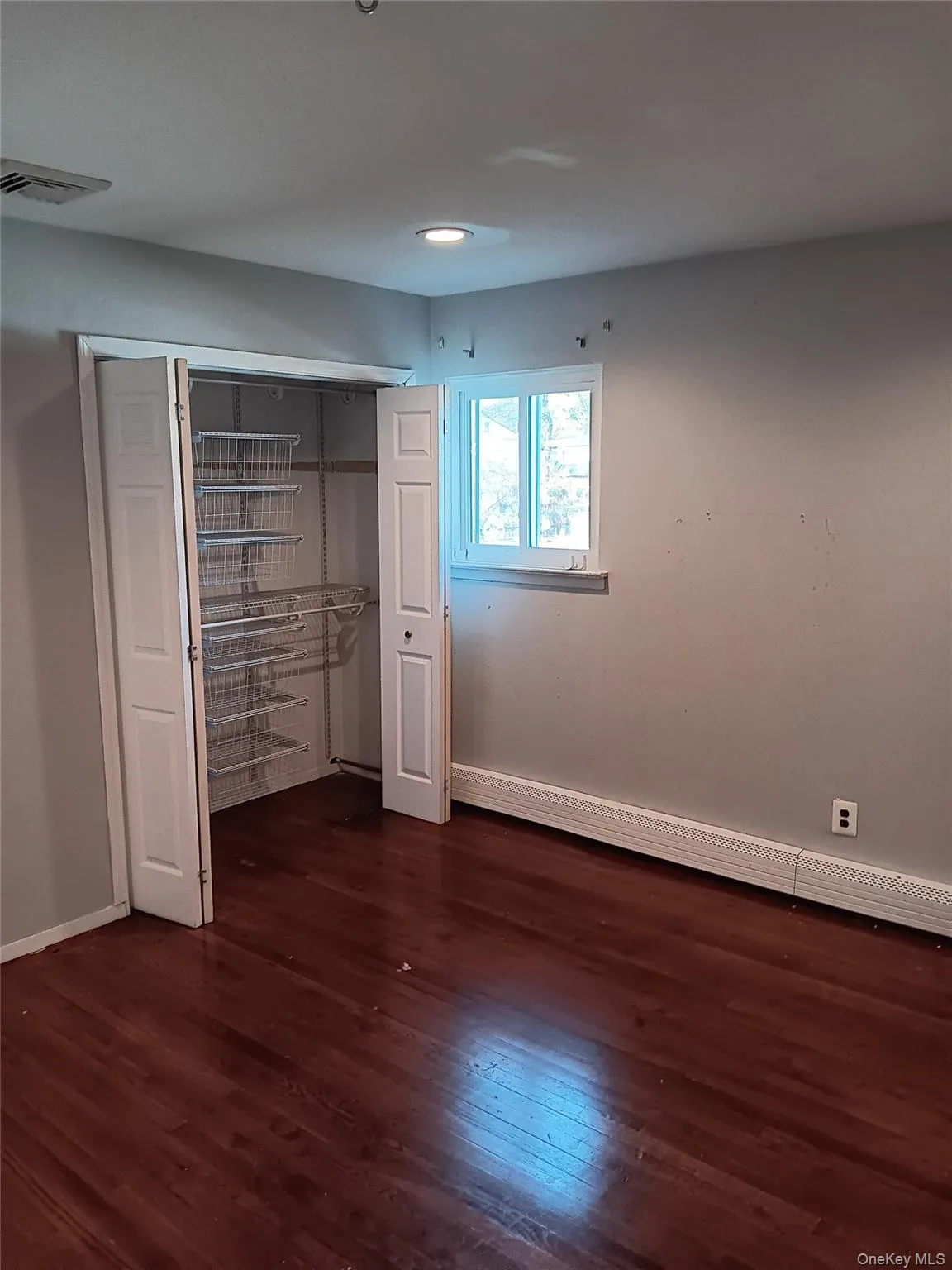 Unfurnished bedroom with a closet, dark wood finished floors, and baseboard heating Unfurnished bedroom with a closet, dark wood finished floors, and baseboard heating