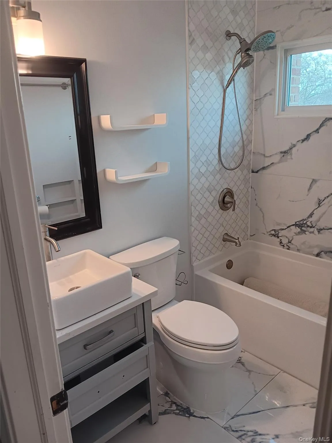 Bathroom with bathing tub / shower combination, vanity, and marble look tiles Bathroom with bathing tub / shower combination, vanity, and marble look tiles