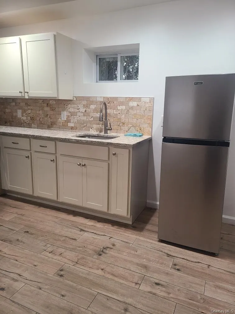 Kitchen featuring freestanding refrigerator, light stone countertops, tasteful backsplash, and light wood-style flooring Kitchen featuring freestanding refrigerator, light stone countertops, tasteful backsplash, and light wood-style flooring