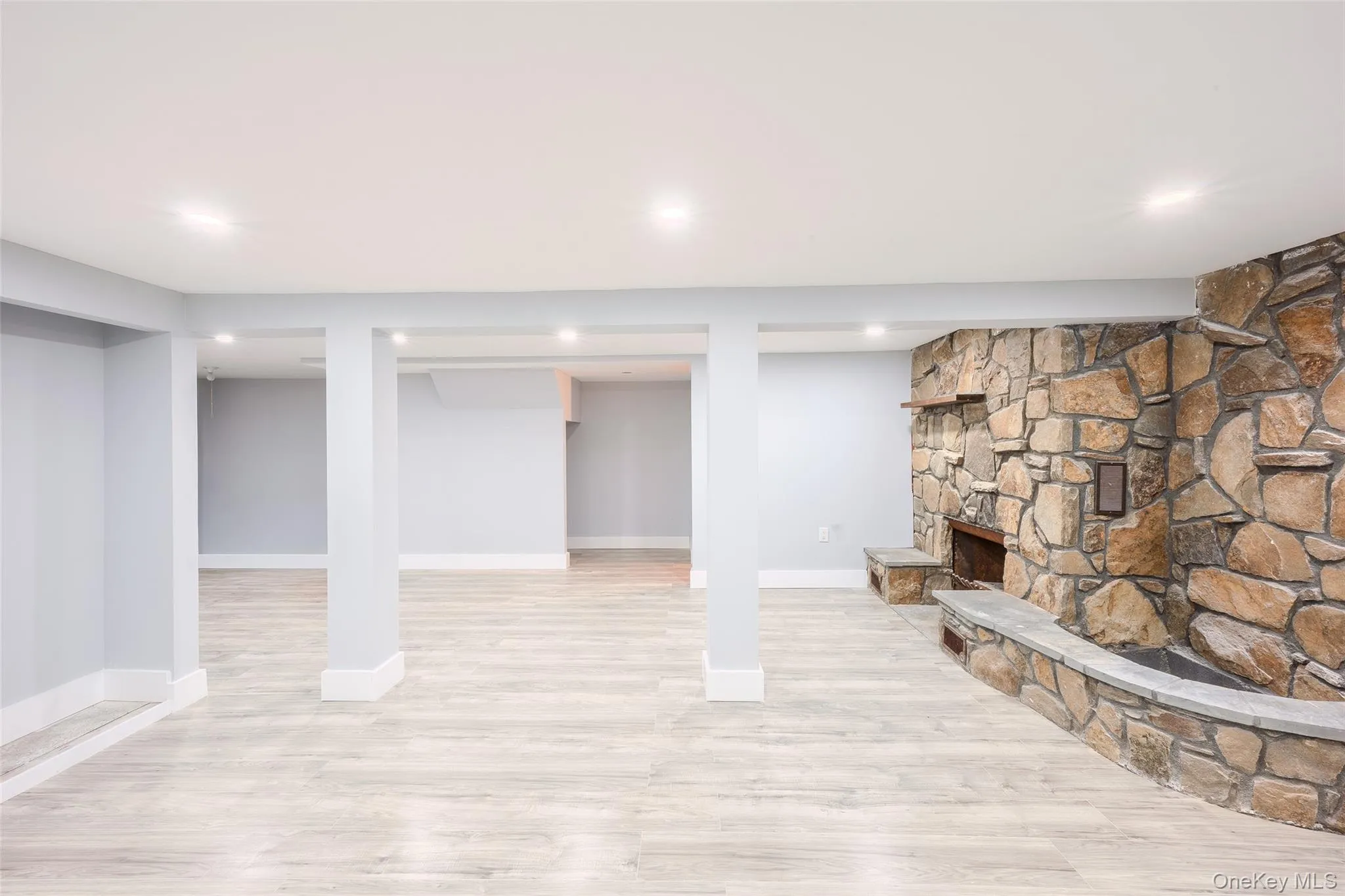 Finished below grade area with light wood finished floors, a stone fireplace, and recessed lighting Finished below grade area with light wood finished floors, a stone fireplace, and recessed lighting
