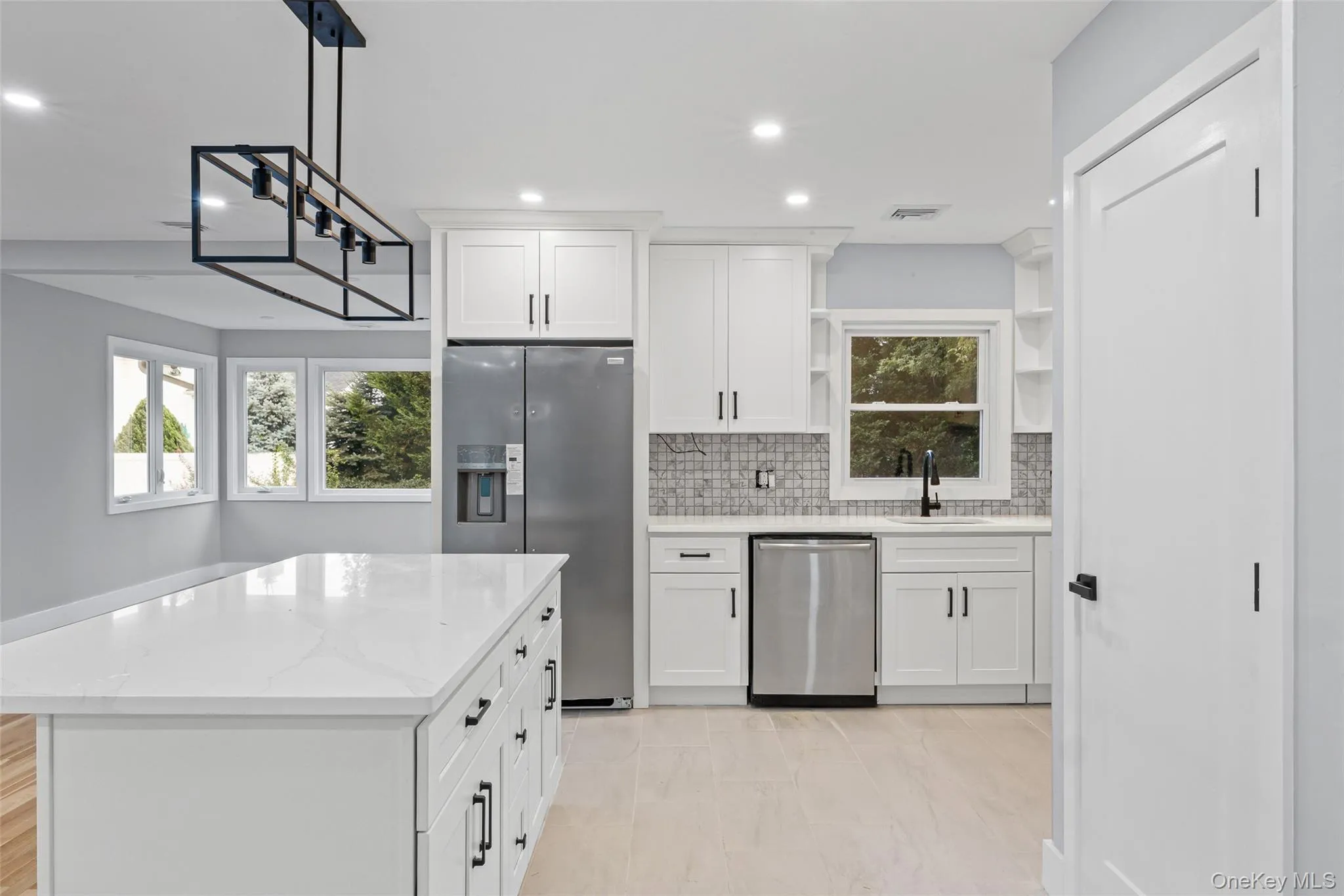 Kitchen with tasteful backsplash, open shelves, appliances with stainless steel finishes, white cabinets, and hanging light fixtures Kitchen with tasteful backsplash, open shelves, appliances with stainless steel finishes, white cabinets, and hanging light fixtures