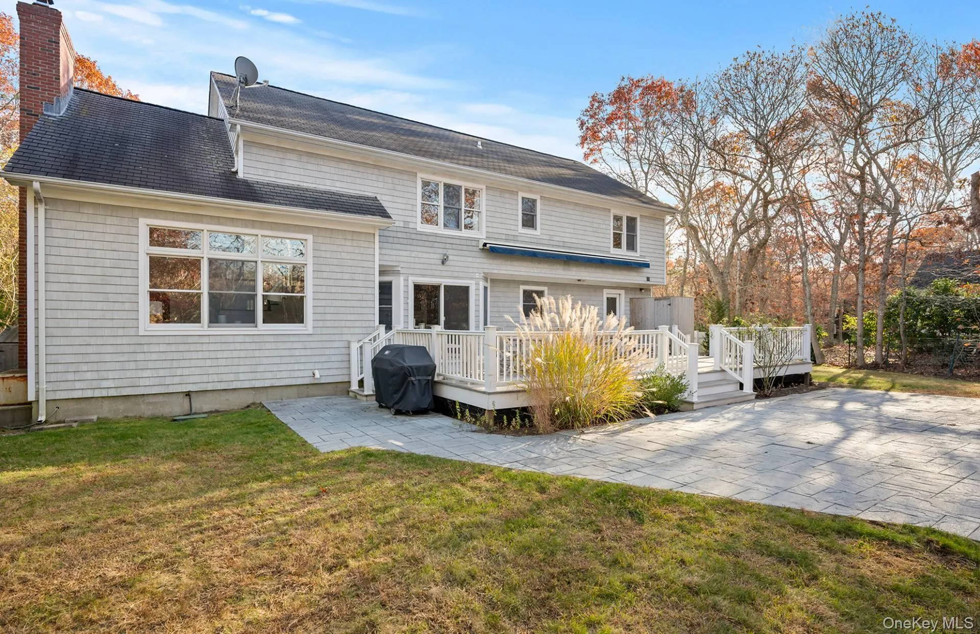 Back of property featuring a yard, a chimney, a wooden deck, a patio, and roof with shingles Back of property featuring a yard, a chimney, a wooden deck, a patio, and roof with shingles