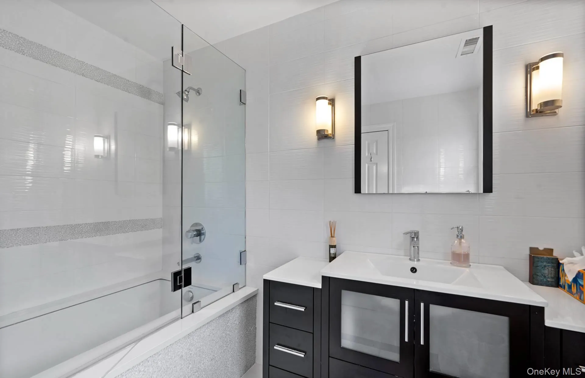 Bathroom with vanity, bath / shower combo with glass door, and tile walls Bathroom with vanity, bath / shower combo with glass door, and tile walls