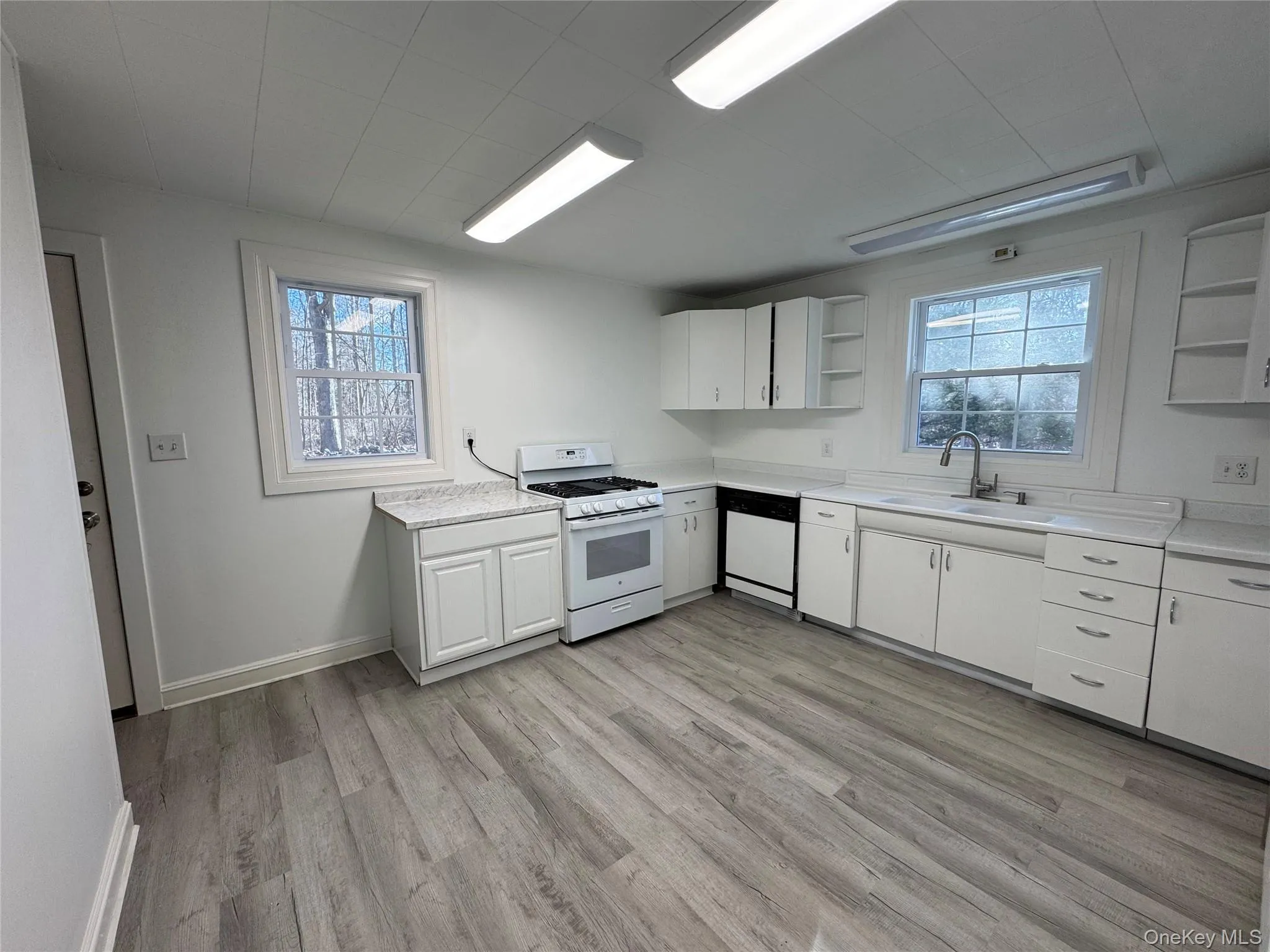 Kitchen featuring open shelves, white cabinets, white appliances, light countertops, and light wood finished floors Kitchen featuring open shelves, white cabinets, white appliances, light countertops, and light wood finished floors