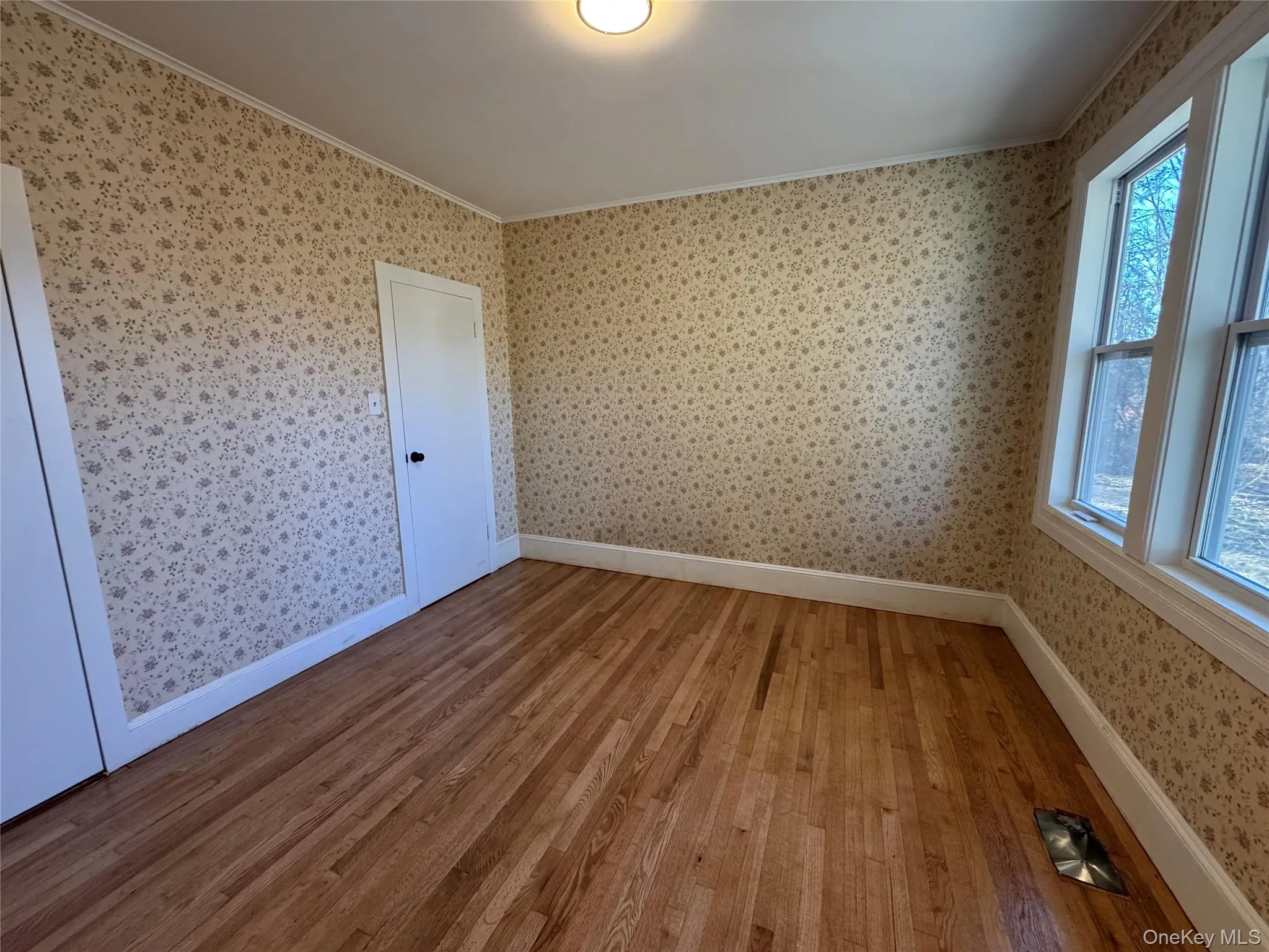 Empty room with hardwood / wood-style floors, crown molding, and wallpapered walls Empty room with hardwood / wood-style floors, crown molding, and wallpapered walls