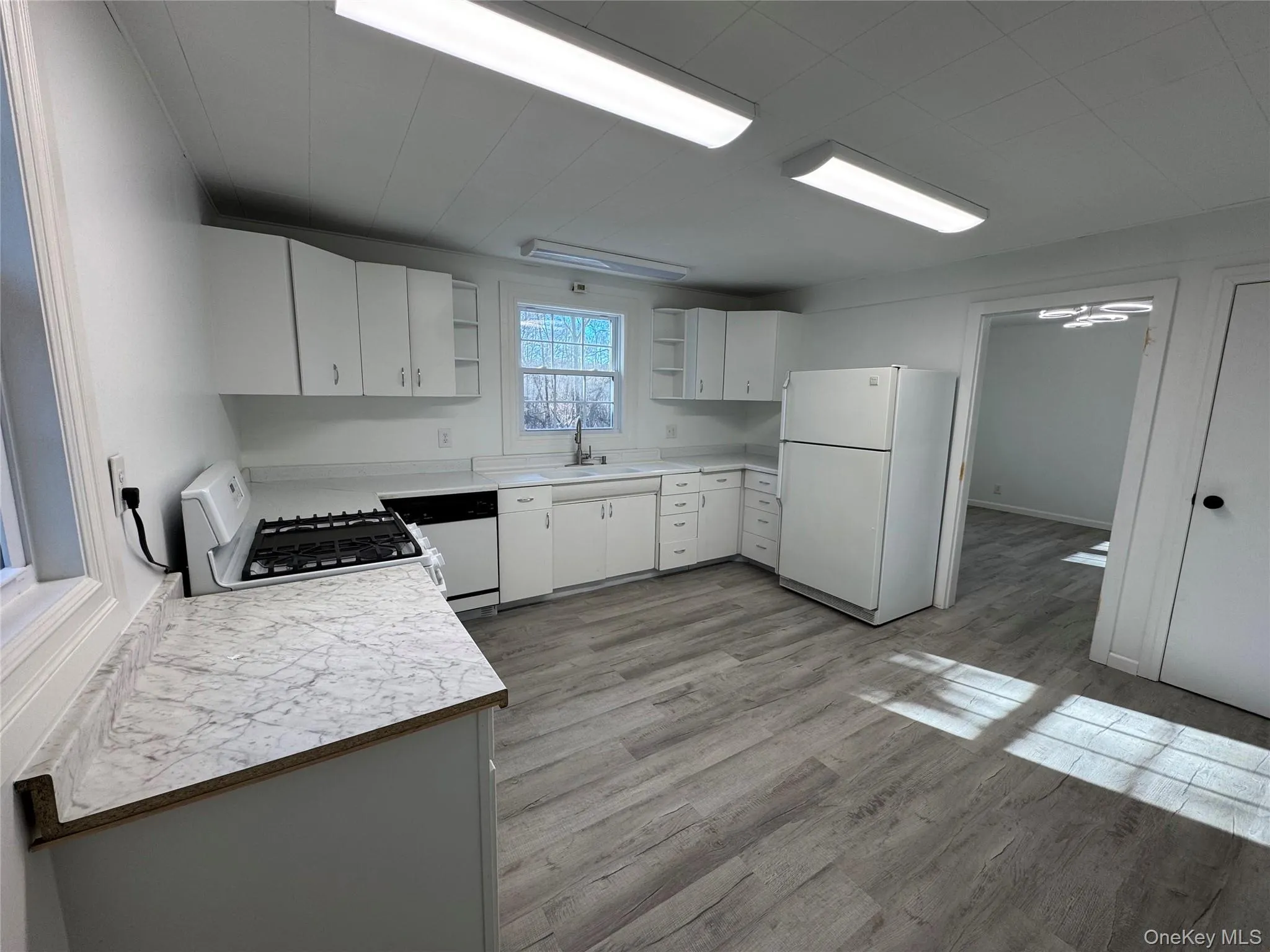 Kitchen featuring light countertops, open shelves, white cabinets, white appliances, and light wood-style floors Kitchen featuring light countertops, open shelves, white cabinets, white appliances, and light wood-style floors
