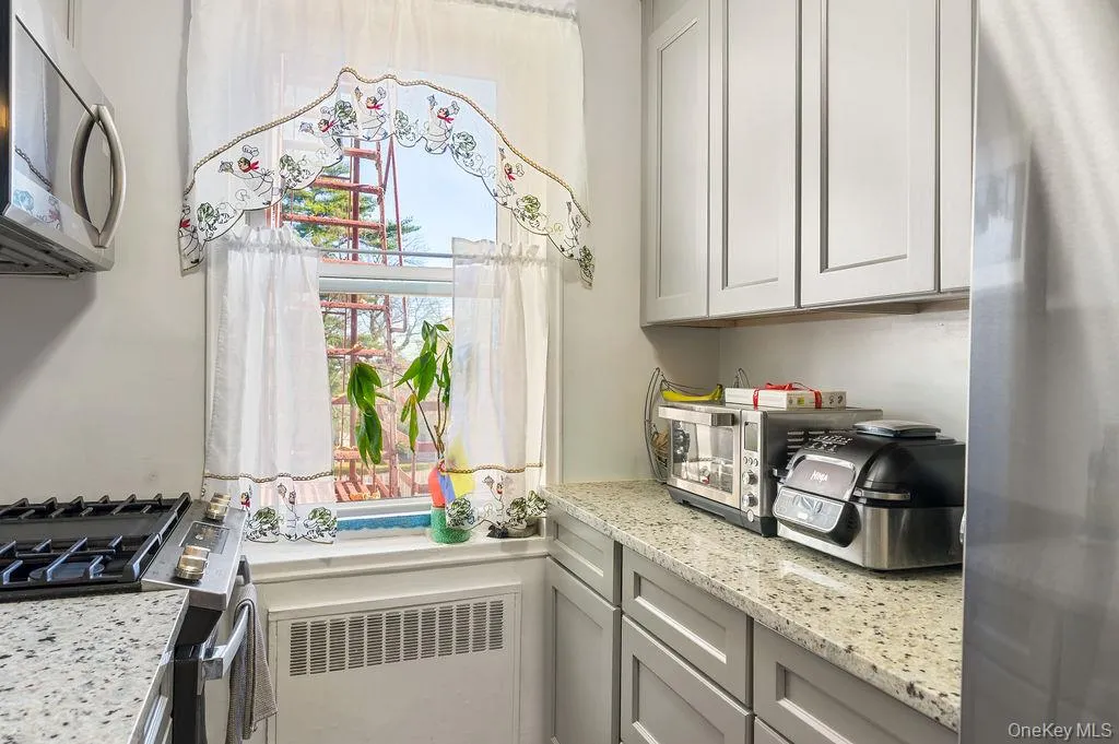 Kitchen with stainless steel appliances, light stone countertops, gray cabinetry, and radiator heating unit Kitchen with stainless steel appliances, light stone countertops, gray cabinetry, and radiator heating unit