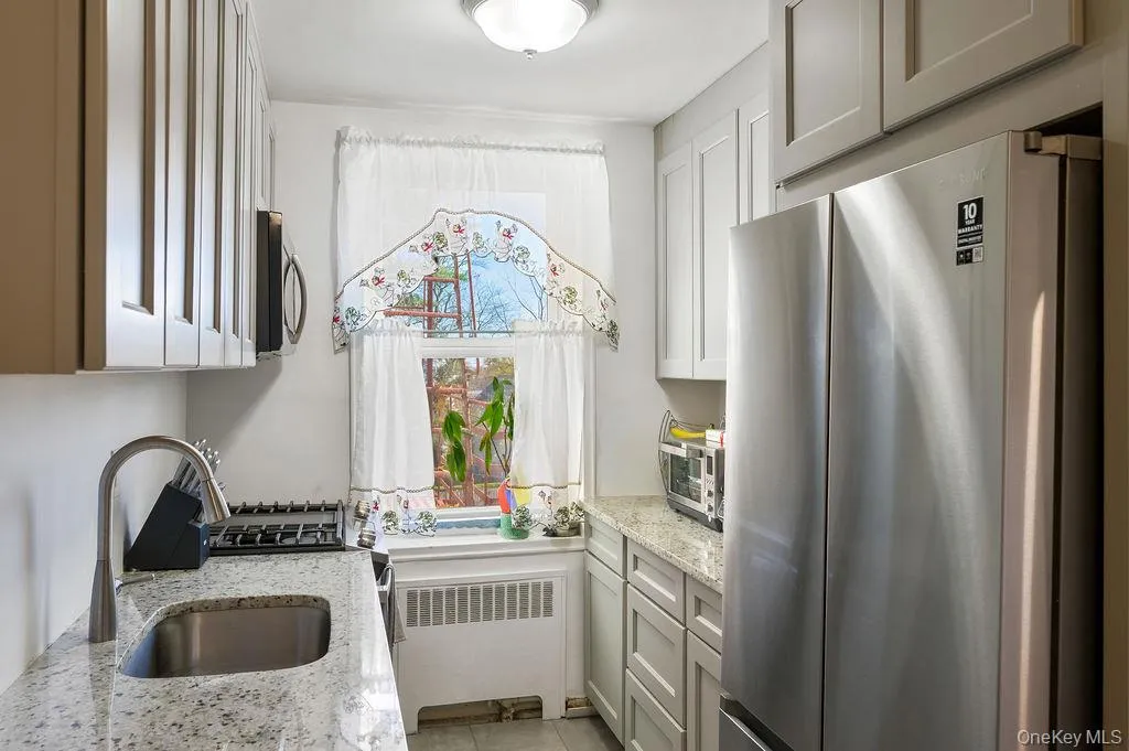 Kitchen with appliances with stainless steel finishes, light stone countertops, and radiator Kitchen with appliances with stainless steel finishes, light stone countertops, and radiator