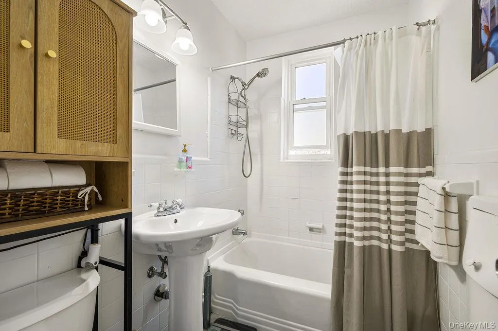 Bathroom with tile walls, shower / bath combination with curtain, and a wainscoted wall Bathroom with tile walls, shower / bath combination with curtain, and a wainscoted wall