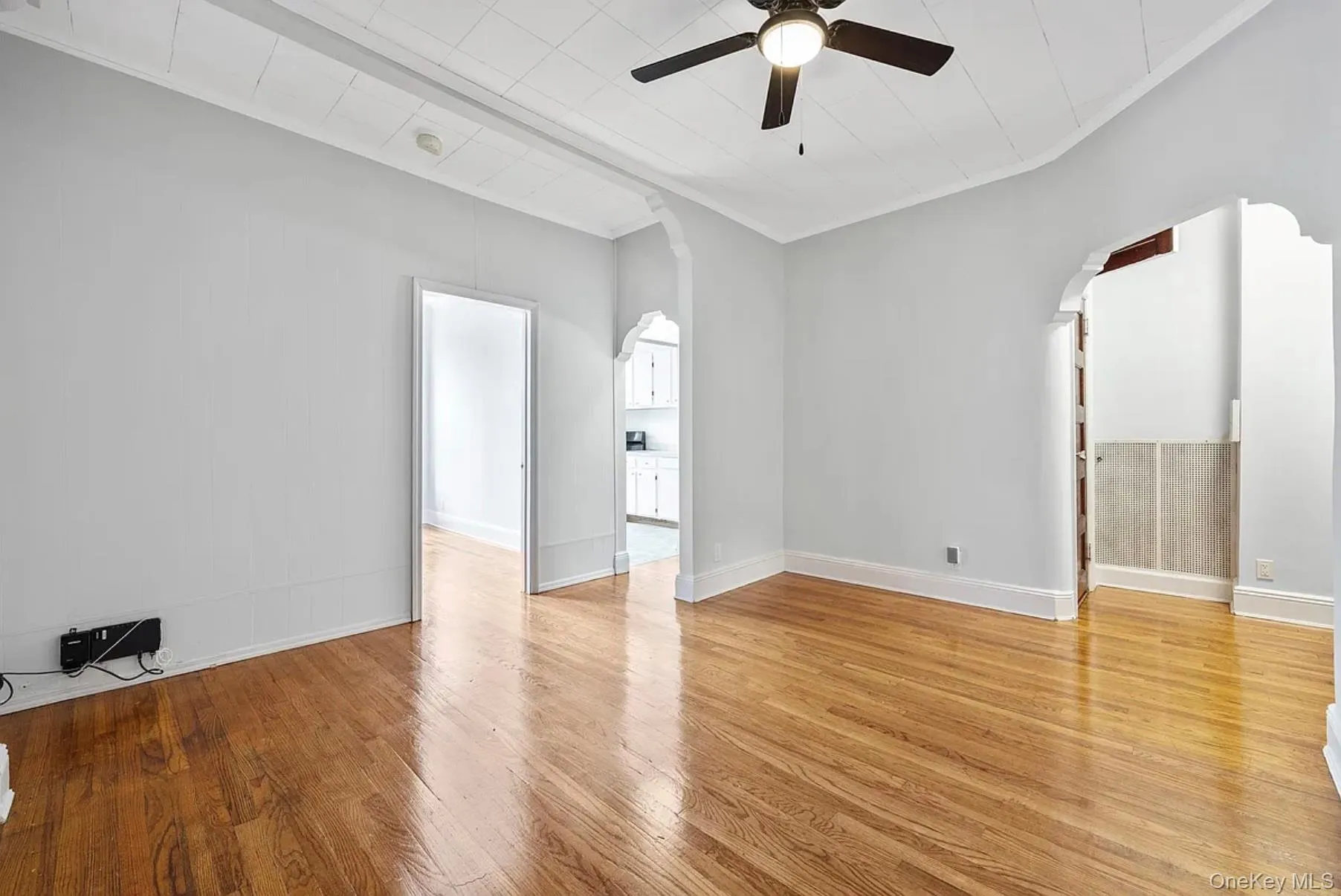 Empty room featuring arched walkways, light wood-style flooring, ornamental molding, and a ceiling fan Empty room featuring arched walkways, light wood-style flooring, ornamental molding, and a ceiling fan