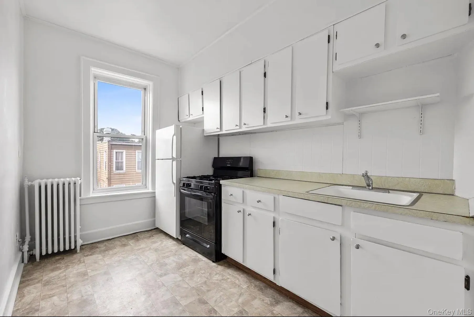 Kitchen featuring gas stove, light countertops, radiator heating unit, white cabinets, and freestanding refrigerator Kitchen featuring gas stove, light countertops, radiator heating unit, white cabinets, and freestanding refrigerator