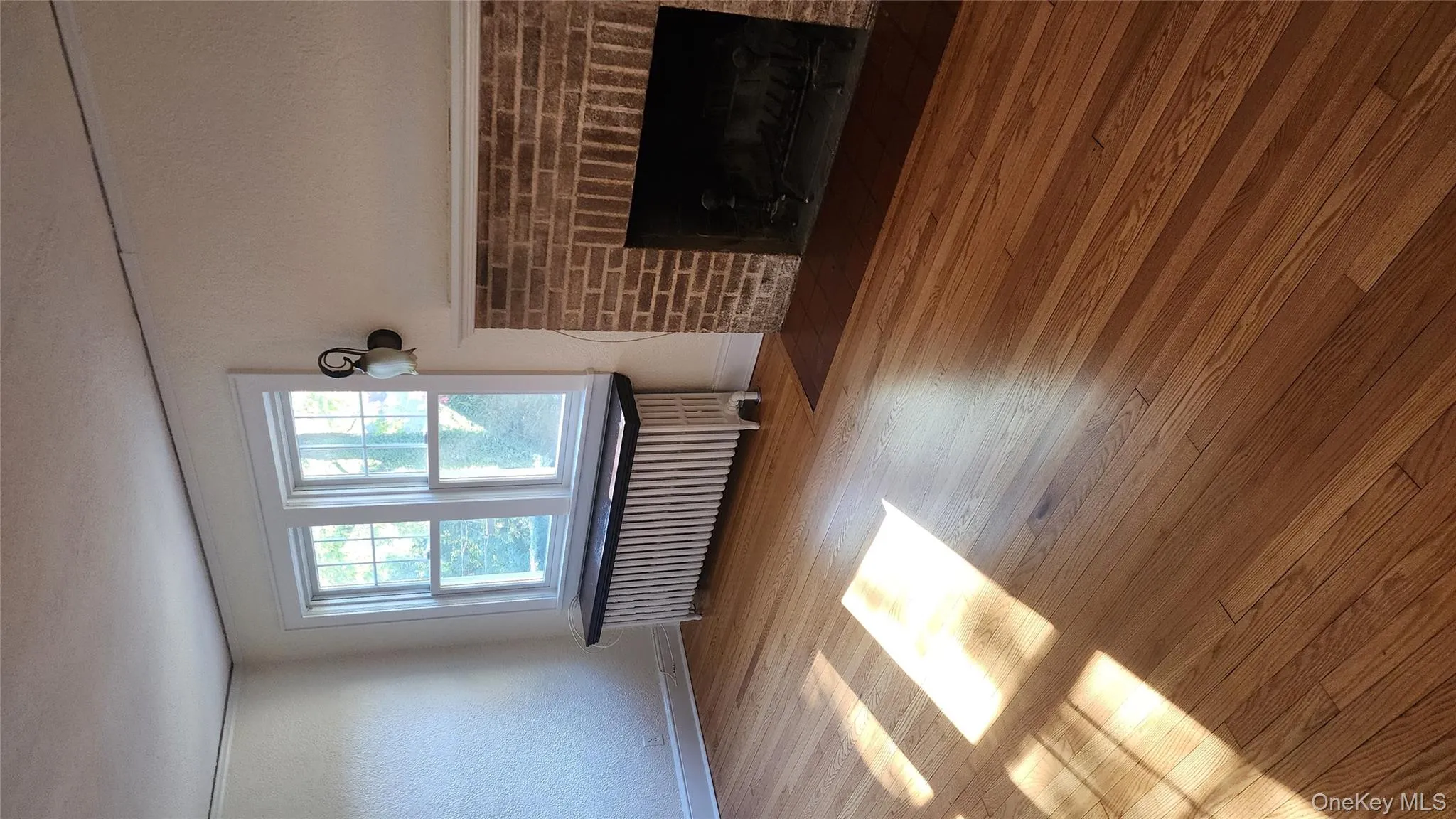 Unfurnished living room with a brick fireplace, radiator, hardwood / wood-style floors, and a textured wall Unfurnished living room with a brick fireplace, radiator, hardwood / wood-style floors, and a textured wall