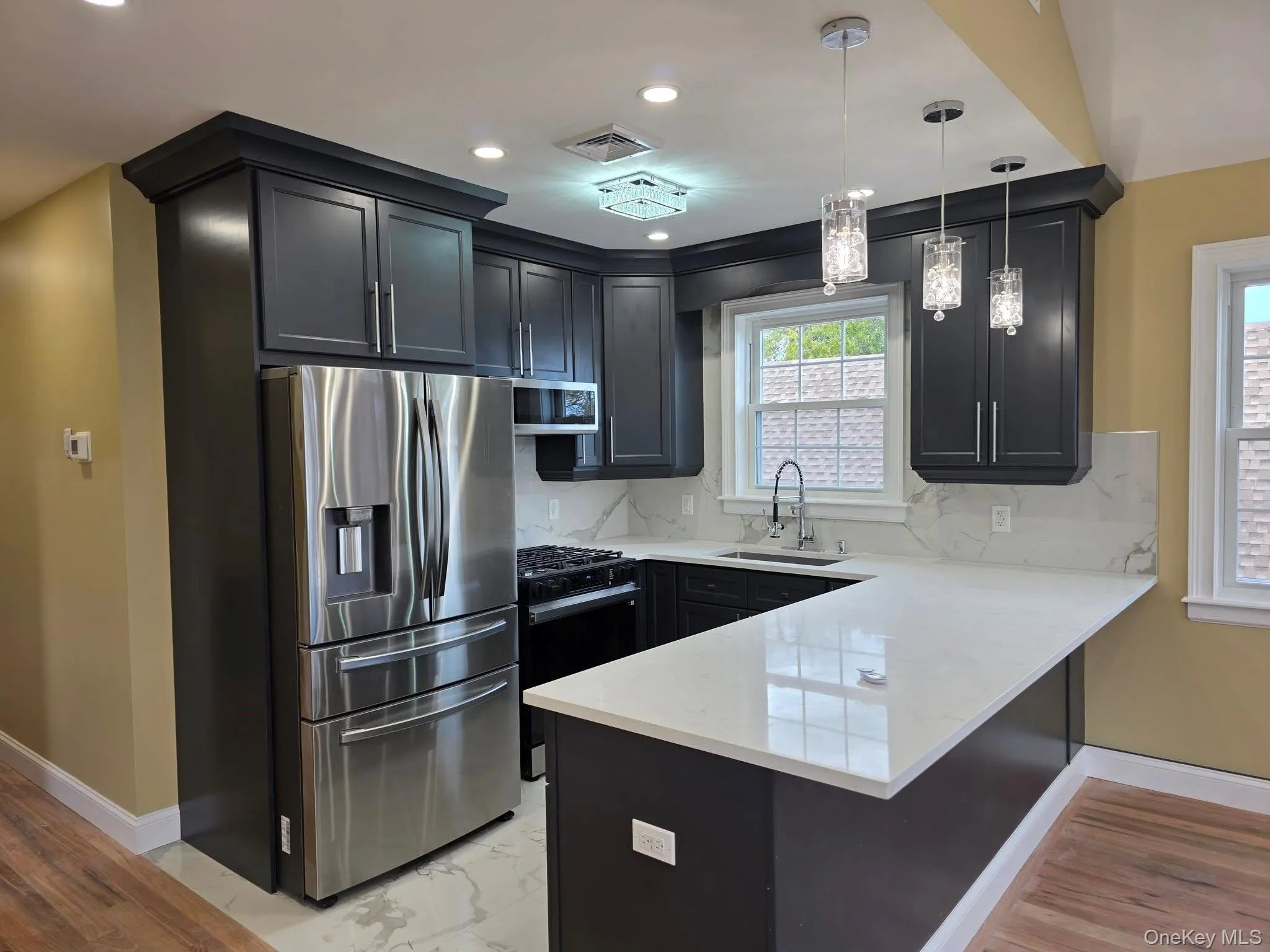 Kitchen with appliances with stainless steel finishes, light stone counters, tasteful backsplash, decorative light fixtures, and recessed lighting Kitchen with appliances with stainless steel finishes, light stone counters, tasteful backsplash, decorative light fixtures, and recessed lighting