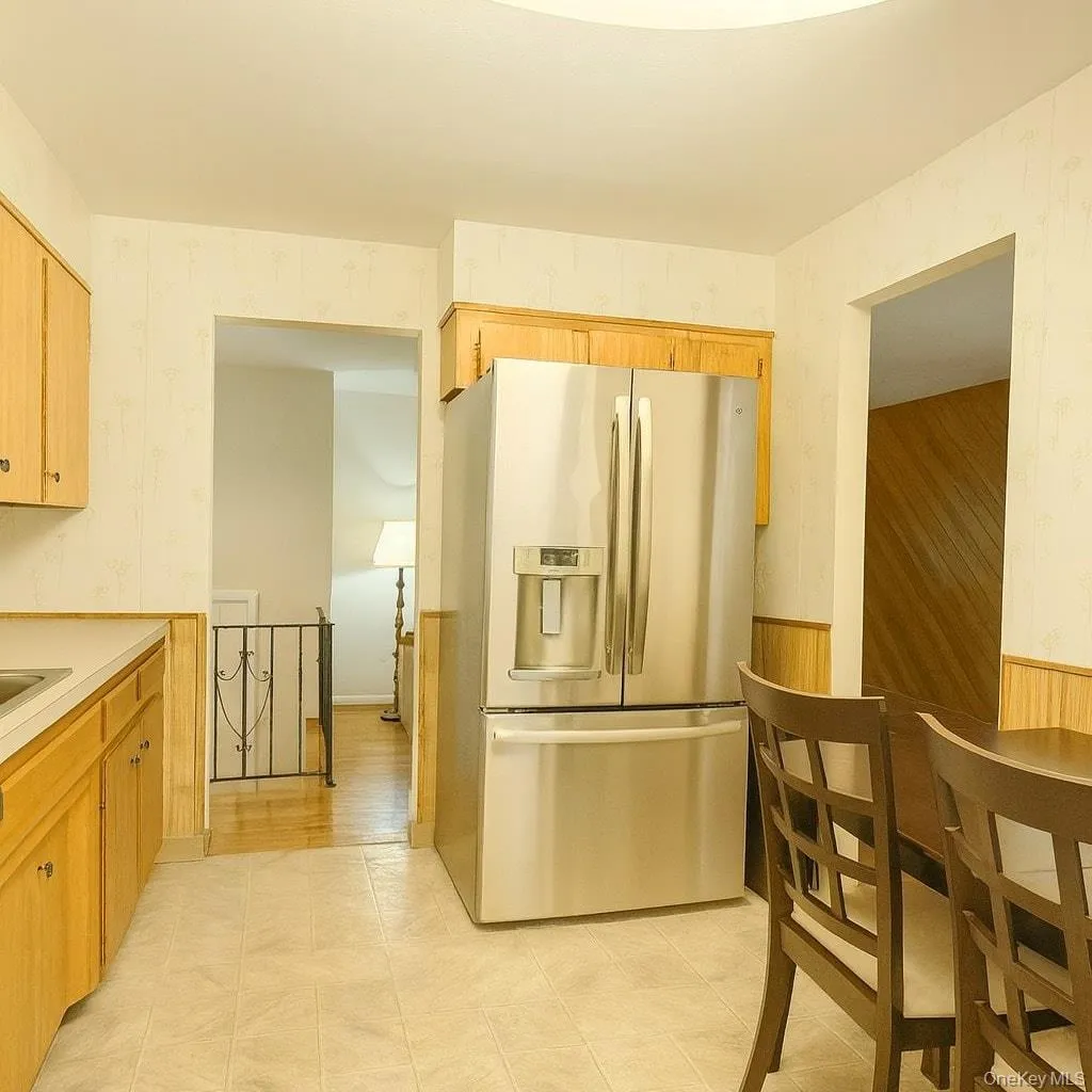 Kitchen with stainless steel refrigerator with ice dispenser, wallpapered walls, light countertops, a wainscoted wall, and light brown cabinetry Kitchen with stainless steel refrigerator with ice dispenser, wallpapered walls, light countertops, a wainscoted wall, and light brown cabinetry