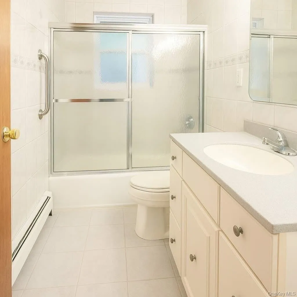 Bathroom with a baseboard heating unit, vanity, tile walls, light tile patterned floors, and shower / bath combination with glass door Bathroom with a baseboard heating unit, vanity, tile walls, light tile patterned floors, and shower / bath combination with glass door
