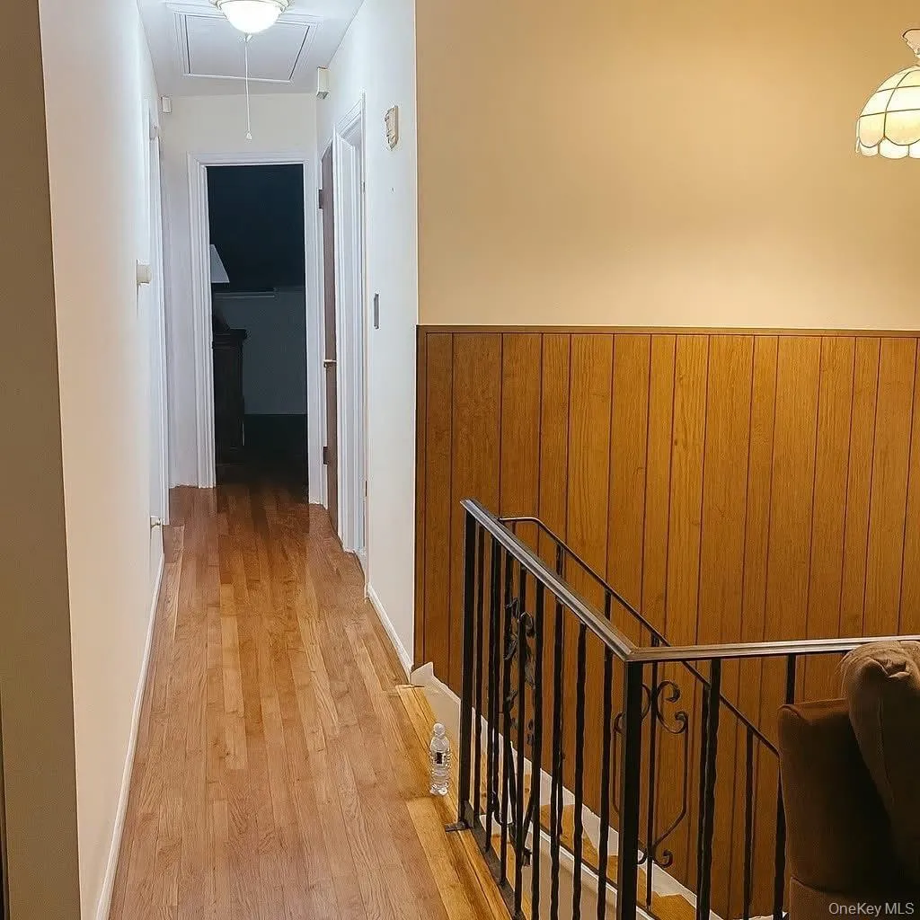 Hallway featuring an upstairs landing, attic access, wood walls, and light wood-type flooring Hallway featuring an upstairs landing, attic access, wood walls, and light wood-type flooring
