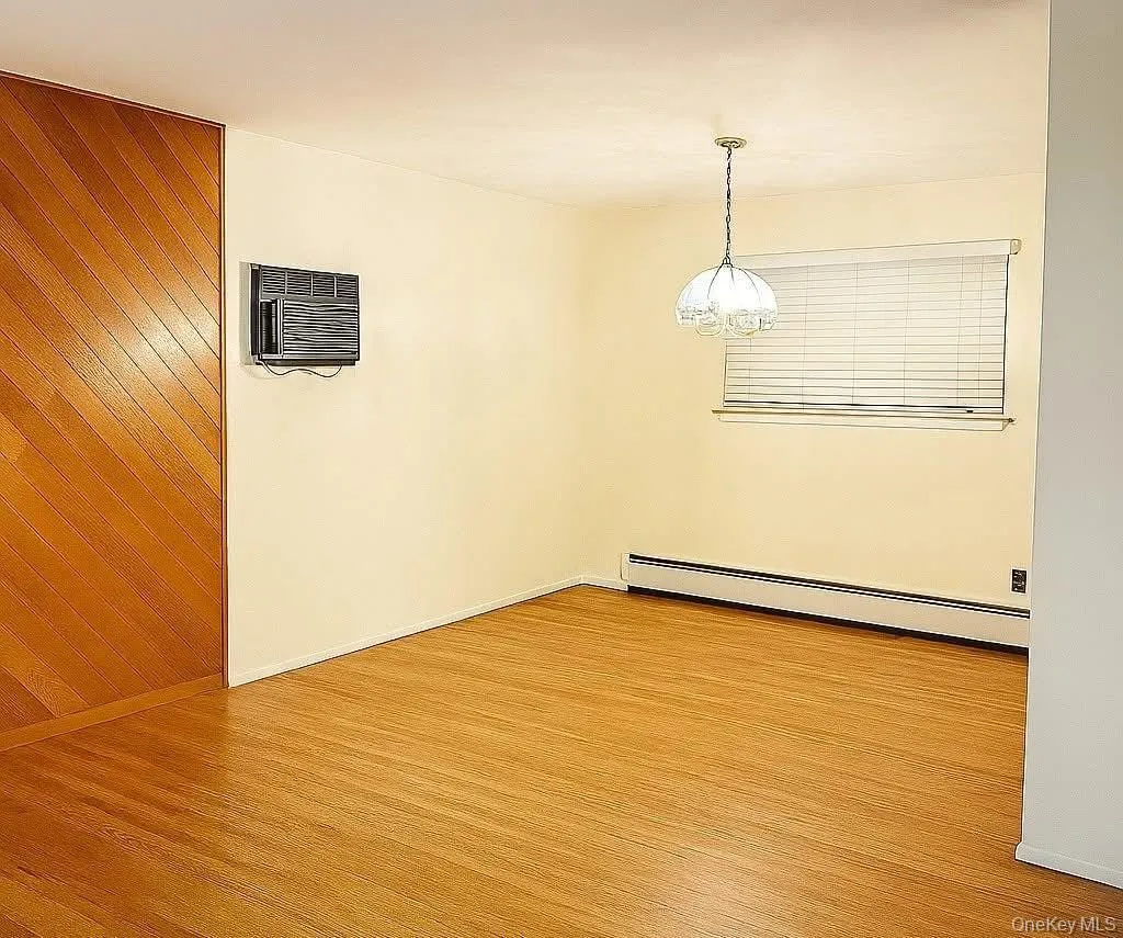 Spare room featuring a baseboard heating unit, light wood finished floors, and a wall mounted air conditioner Spare room featuring a baseboard heating unit, light wood finished floors, and a wall mounted air conditioner