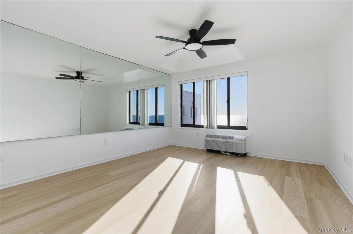 Empty room featuring light wood-style flooring, a ceiling fan, and a wall mounted air conditioner Empty room featuring light wood-style flooring, a ceiling fan, and a wall mounted air conditioner