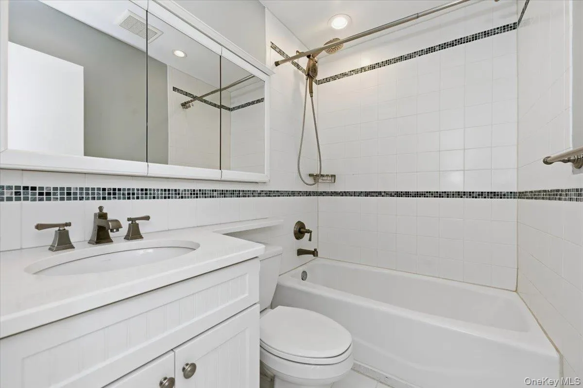 Bathroom with vanity, shower / bath combination, recessed lighting, decorative backsplash, and tile walls Bathroom with vanity, shower / bath combination, recessed lighting, decorative backsplash, and tile walls