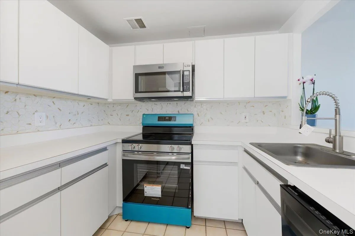 Kitchen featuring stainless steel appliances, white cabinets, light countertops, light tile patterned floors, and backsplash Kitchen featuring stainless steel appliances, white cabinets, light countertops, light tile patterned floors, and backsplash