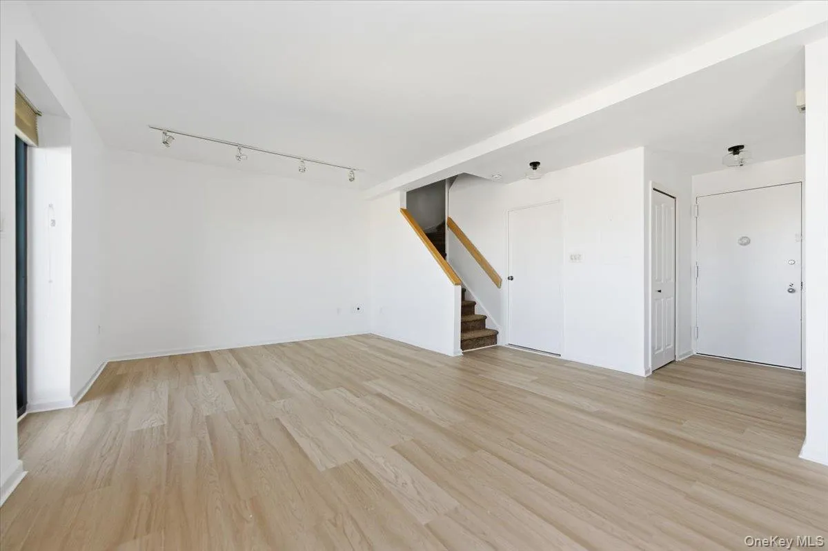 Unfurnished living room featuring stairs, track lighting, and light wood-style floors Unfurnished living room featuring stairs, track lighting, and light wood-style floors