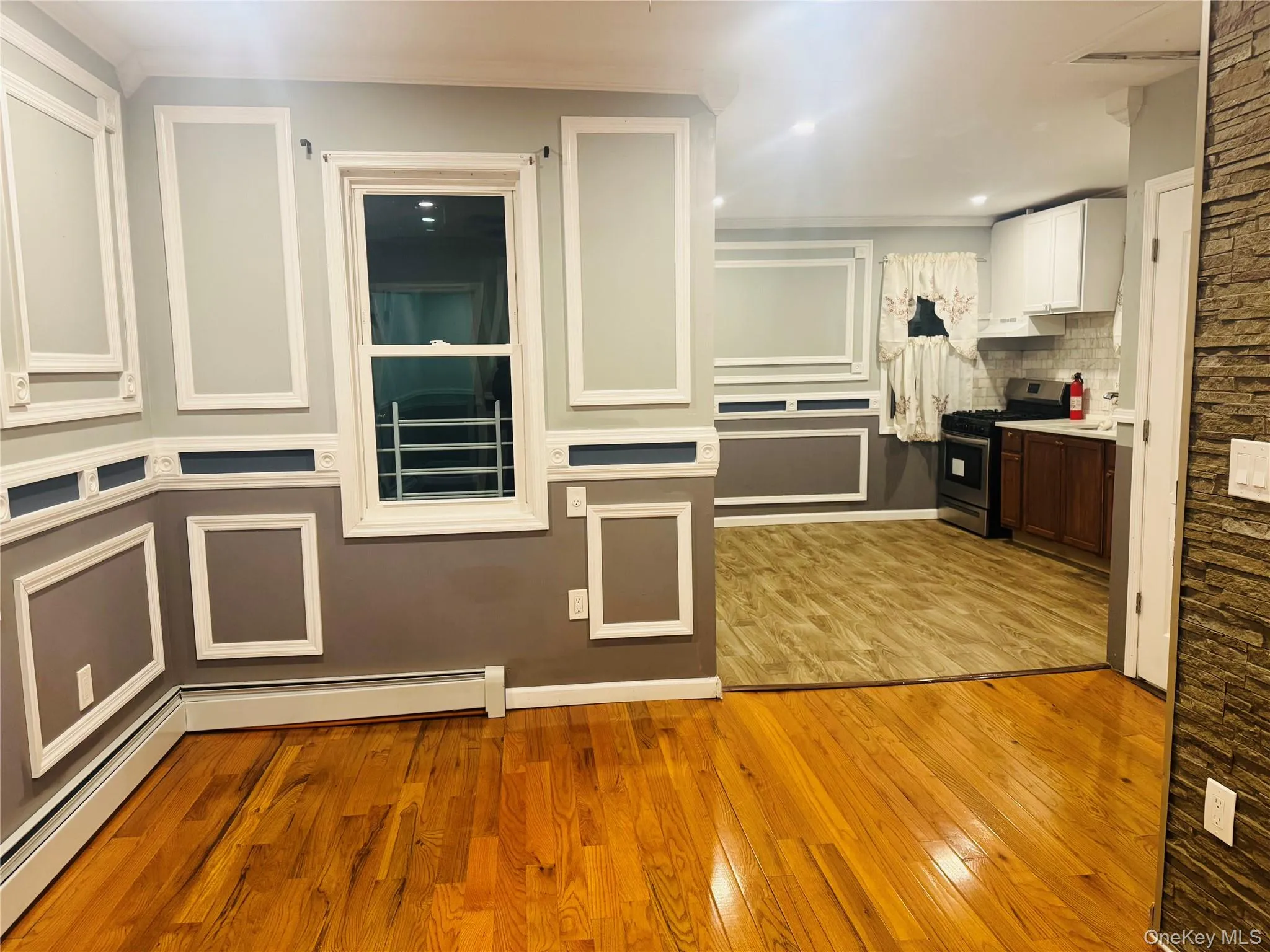 Kitchen with light wood-style floors, baseboard heating, white cabinets, stainless steel gas range, and tasteful backsplash Kitchen with light wood-style floors, baseboard heating, white cabinets, stainless steel gas range, and tasteful backsplash