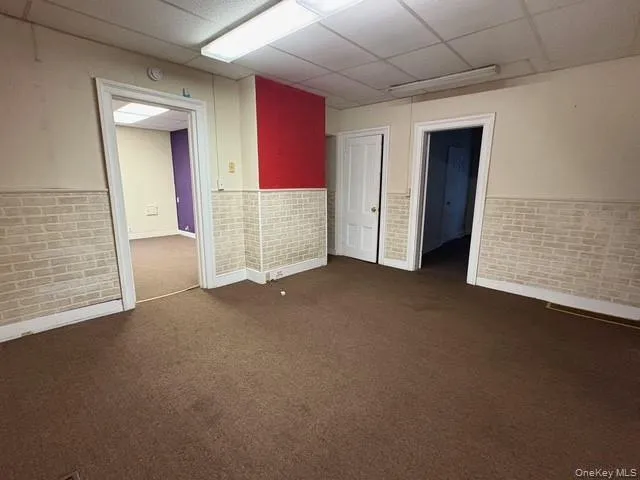 Spare room with a wainscoted wall, brick wall, a drop ceiling, and dark carpet Spare room with a wainscoted wall, brick wall, a drop ceiling, and dark carpet