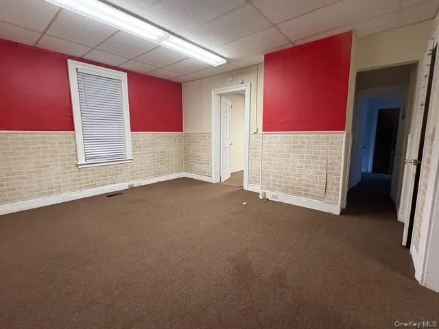 Spare room with a wainscoted wall, brick wall, a paneled ceiling, and dark carpet Spare room with a wainscoted wall, brick wall, a paneled ceiling, and dark carpet