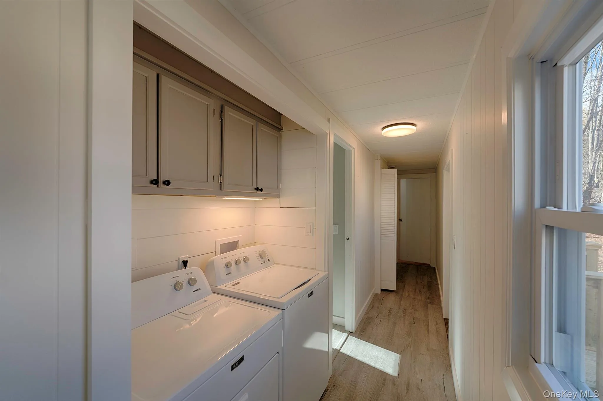 Laundry area featuring cabinet space, washer and dryer, light wood-type flooring, and wood walls Laundry area featuring cabinet space, washer and dryer, light wood-type flooring, and wood walls