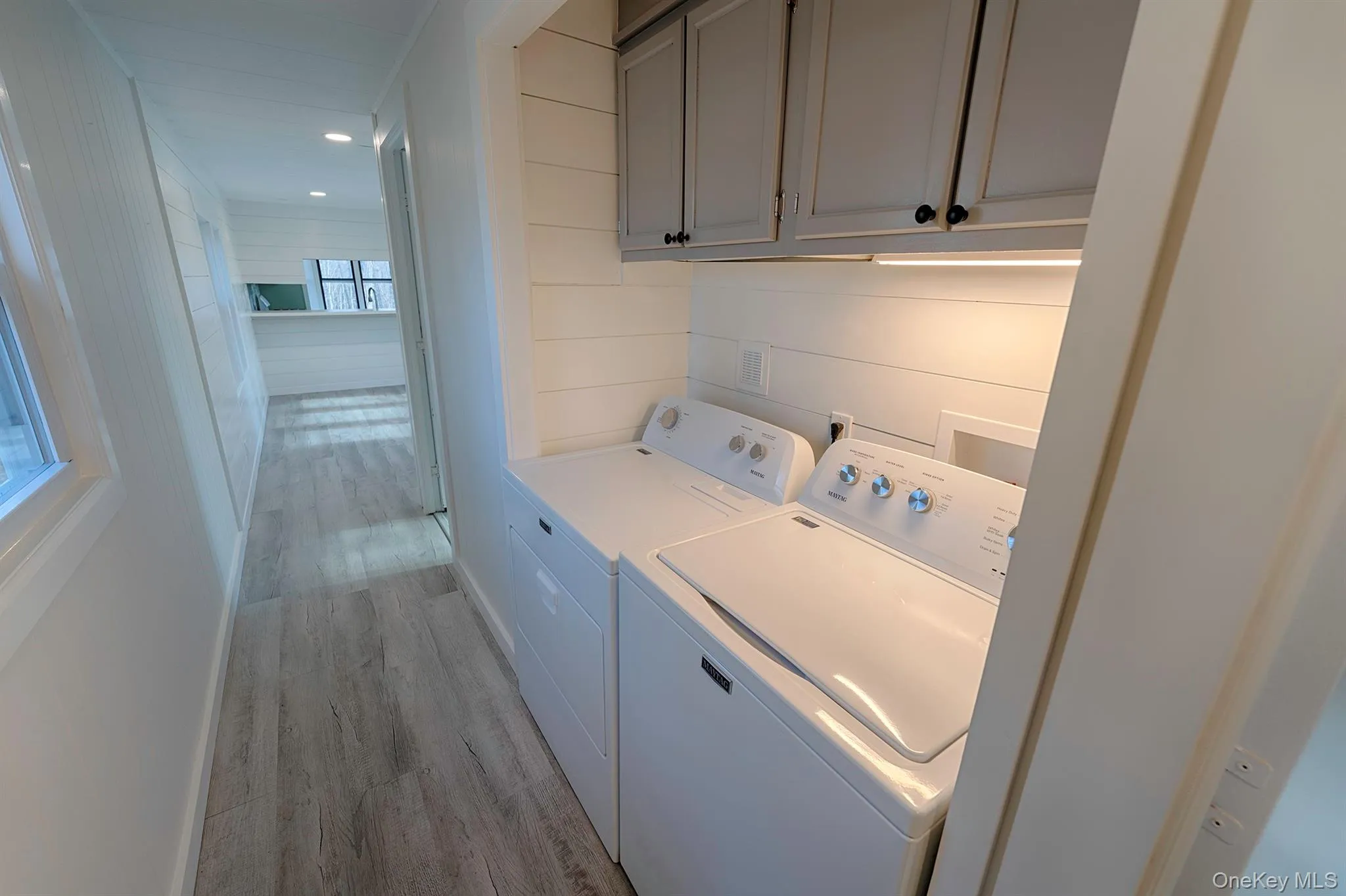 Washroom with light wood finished floors, cabinet space, washing machine and clothes dryer, wooden walls, and recessed lighting Washroom with light wood finished floors, cabinet space, washing machine and clothes dryer, wooden walls, and recessed lighting