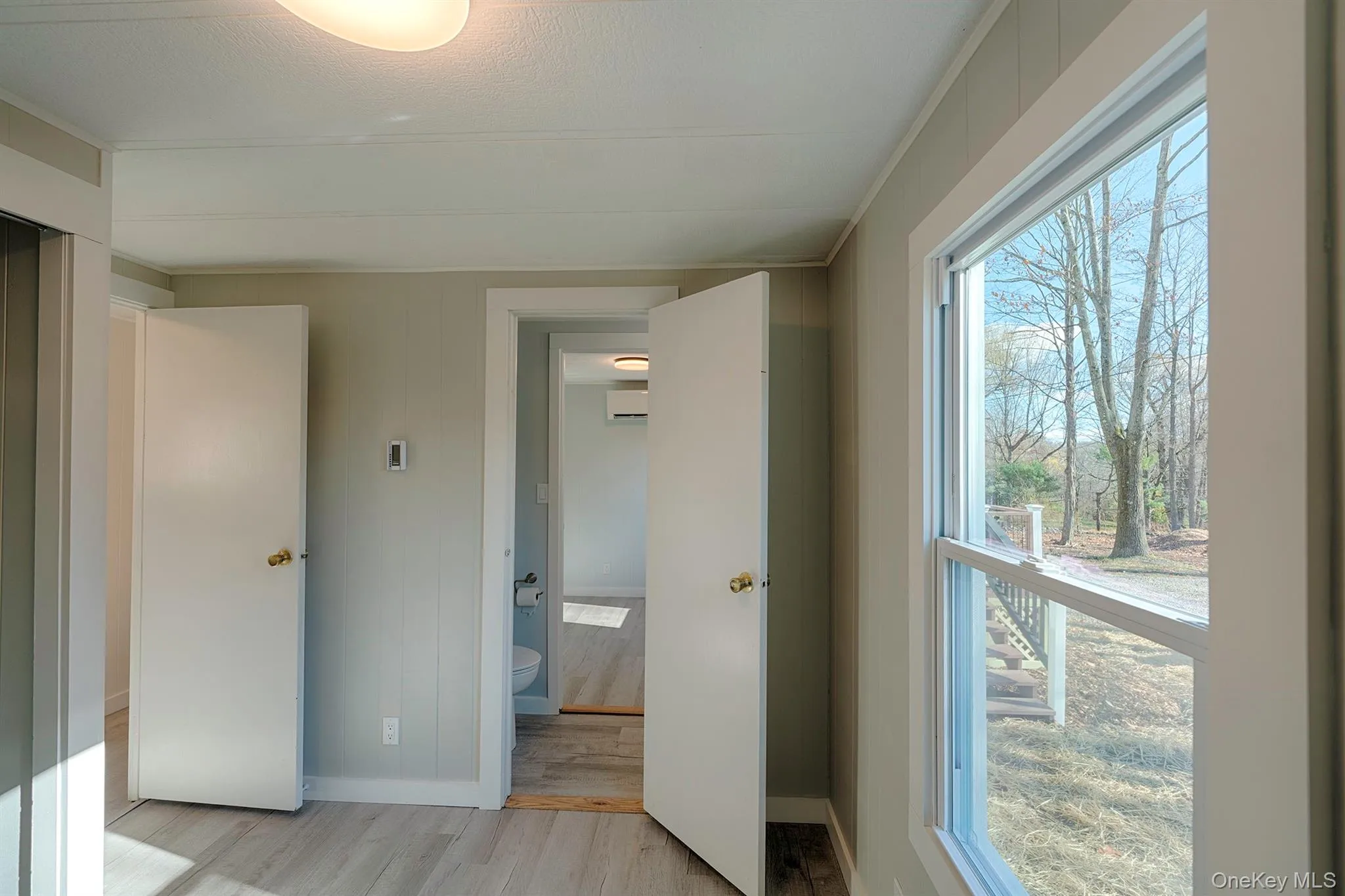 Unfurnished bedroom with light wood-style floors, ensuite bath, a wall mounted AC, and elevator Unfurnished bedroom with light wood-style floors, ensuite bath, a wall mounted AC, and elevator