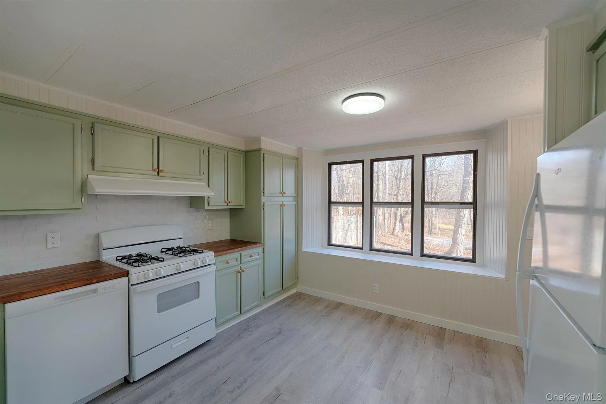 Kitchen featuring green cabinetry, white appliances, under cabinet range hood, light wood-type flooring, and backsplash Kitchen featuring green cabinetry, white appliances, under cabinet range hood, light wood-type flooring, and backsplash