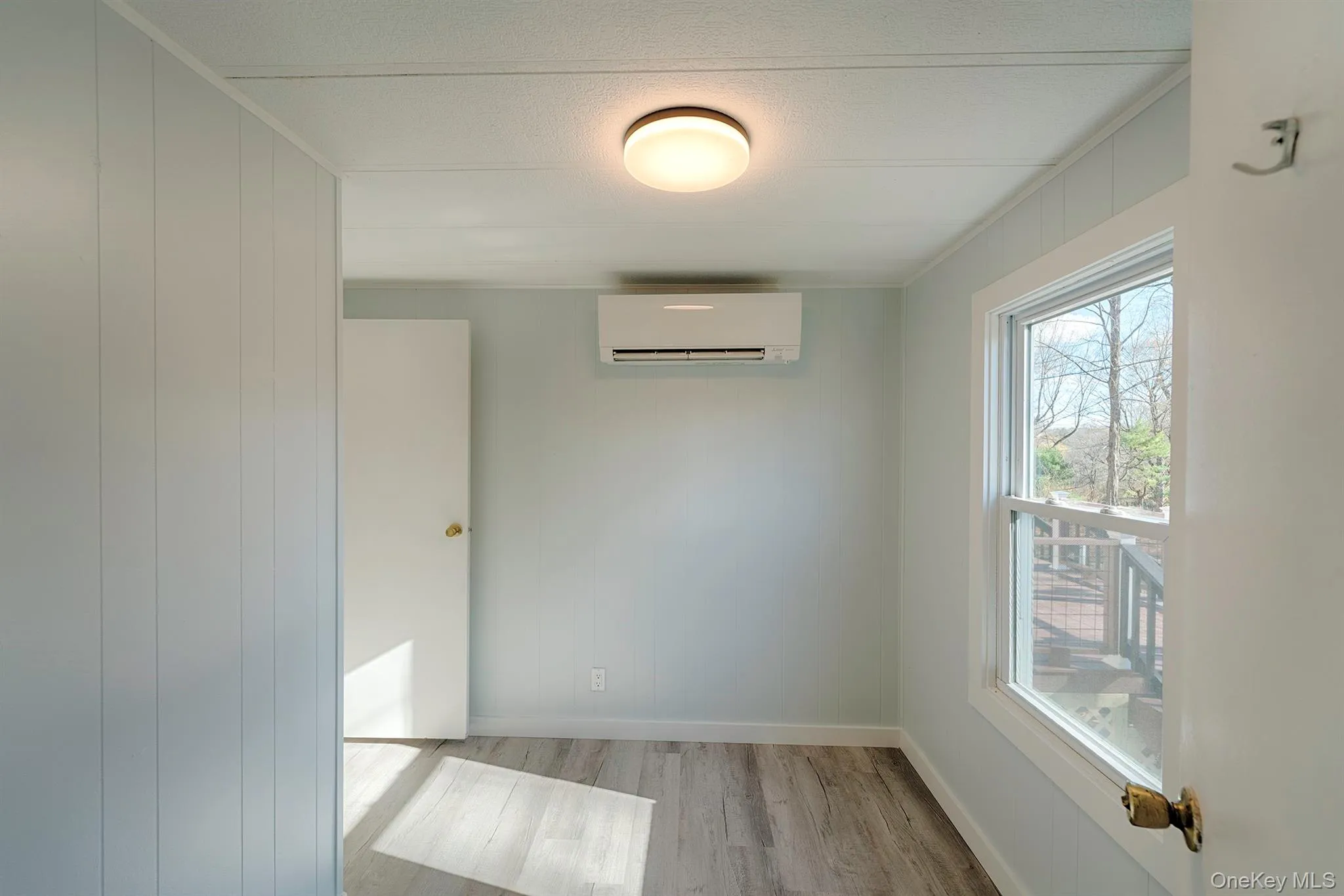 Spare room with light wood finished floors, a wall unit AC, and wooden walls Spare room with light wood finished floors, a wall unit AC, and wooden walls