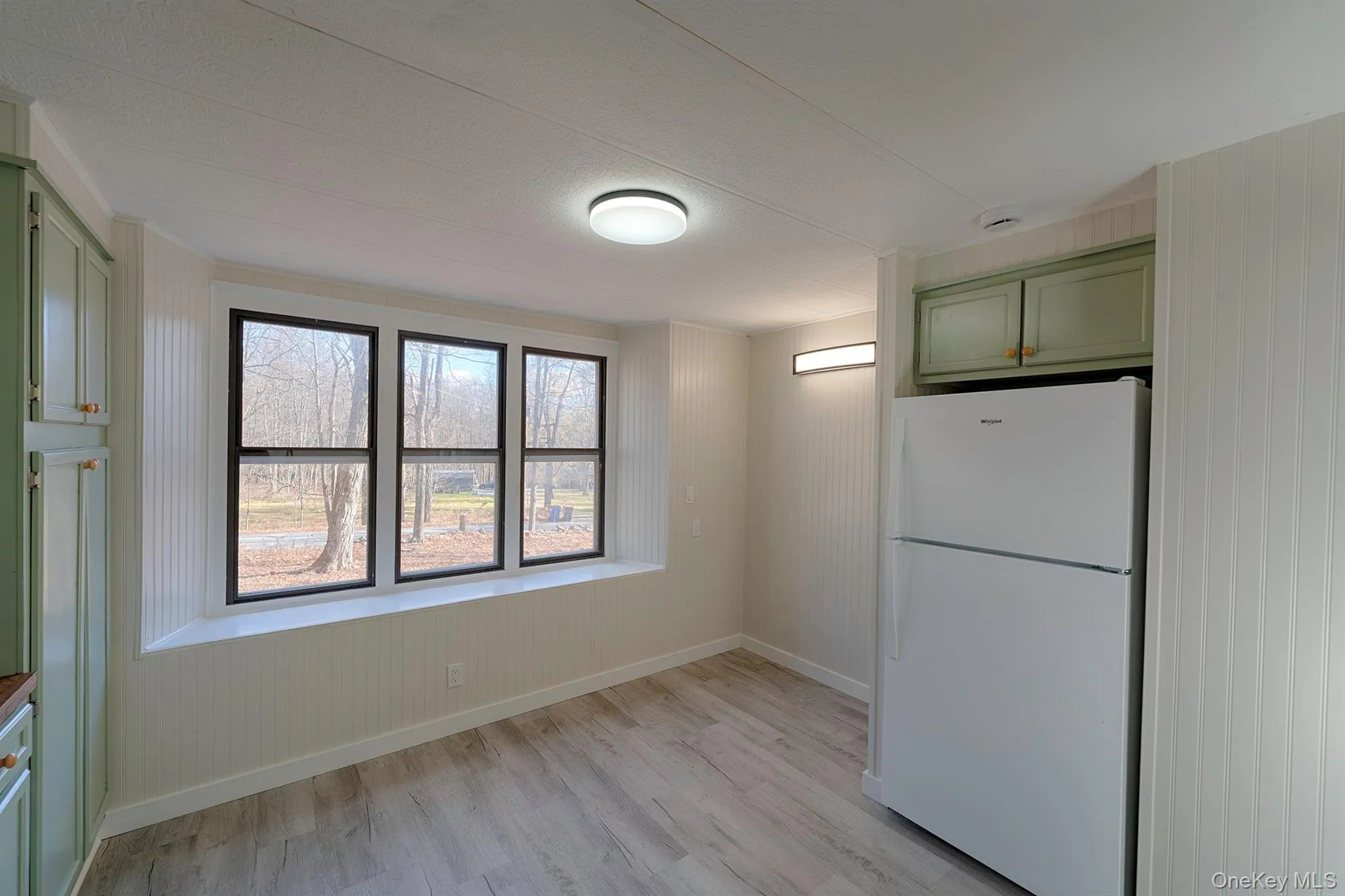 Kitchen featuring green cabinets, freestanding refrigerator, light wood-type flooring, and wood walls Kitchen featuring green cabinets, freestanding refrigerator, light wood-type flooring, and wood walls
