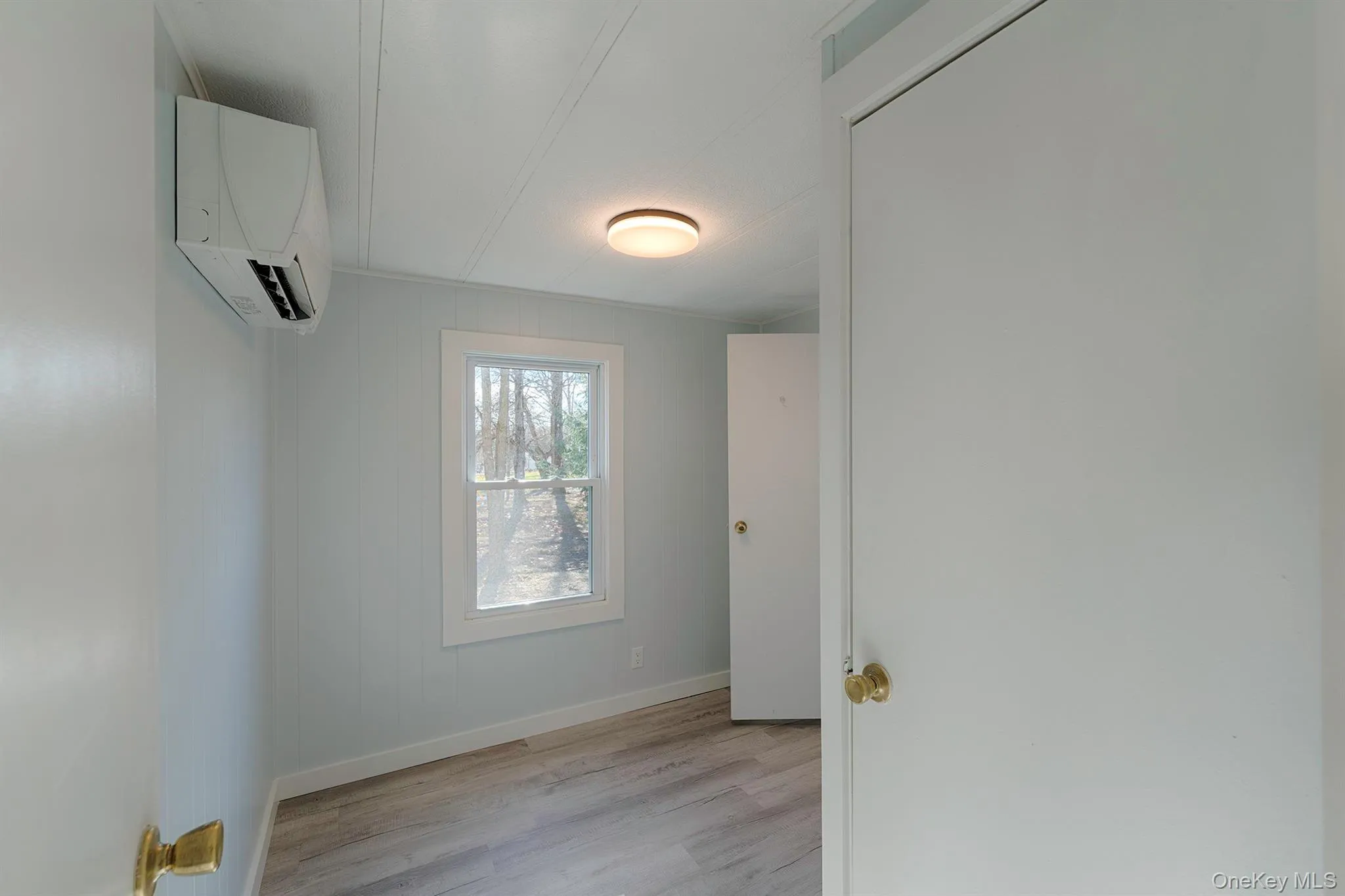 Empty room with light wood finished floors, a wall unit AC, and wooden walls Empty room with light wood finished floors, a wall unit AC, and wooden walls