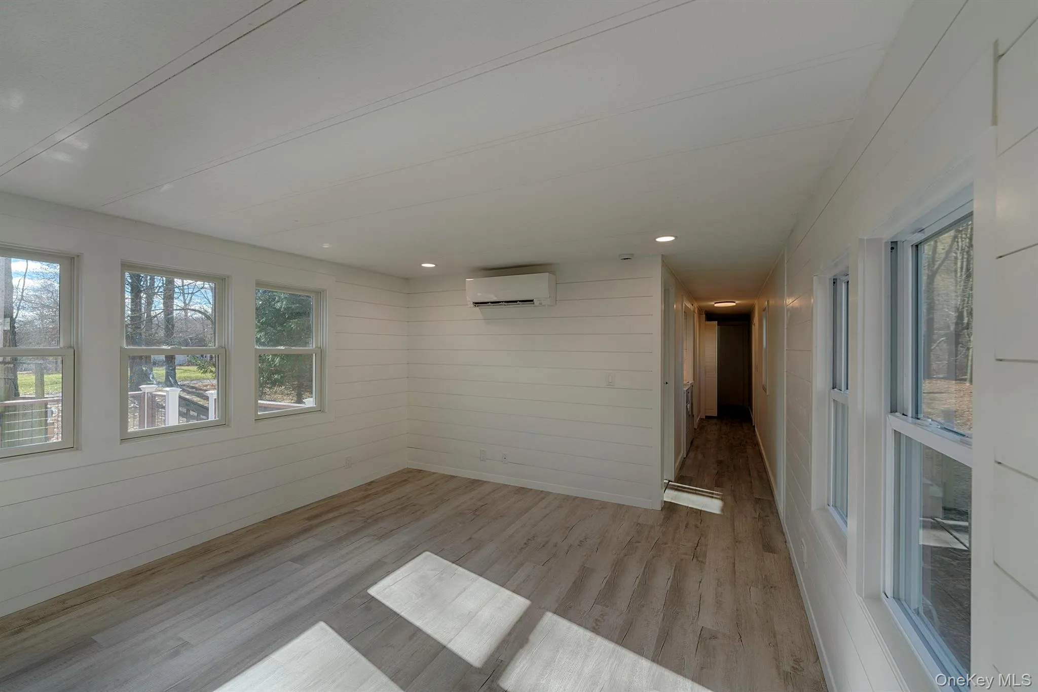 Empty room featuring light wood-type flooring, wood walls, and a wall mounted air conditioner Empty room featuring light wood-type flooring, wood walls, and a wall mounted air conditioner