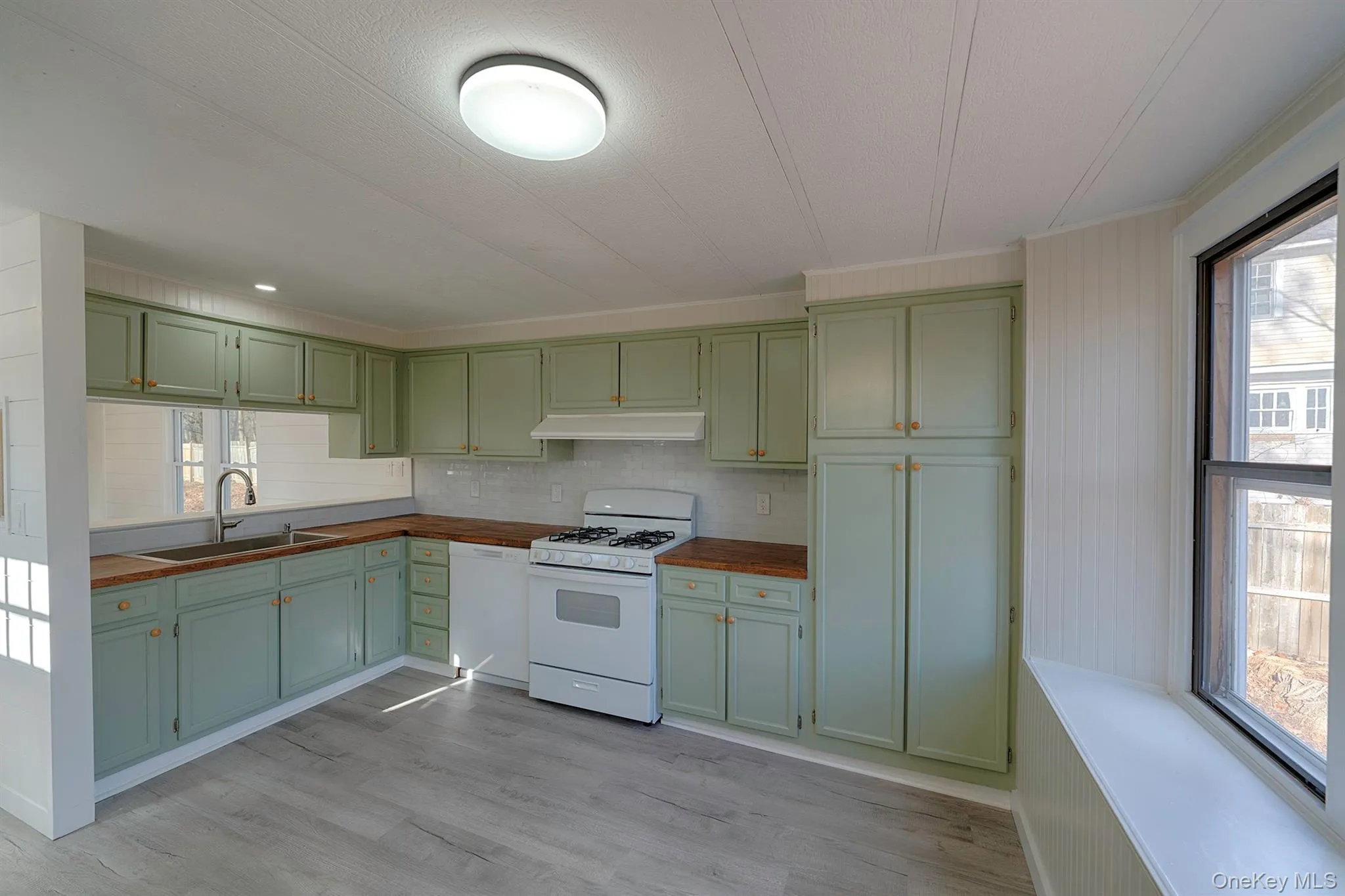 Kitchen featuring white appliances, green cabinets, dark countertops, and under cabinet range hood Kitchen featuring white appliances, green cabinets, dark countertops, and under cabinet range hood