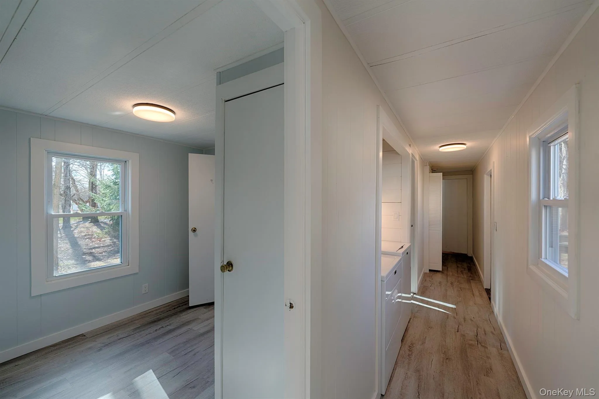 Hall with healthy amount of natural light, light wood-style flooring, and wood walls Hall with healthy amount of natural light, light wood-style flooring, and wood walls