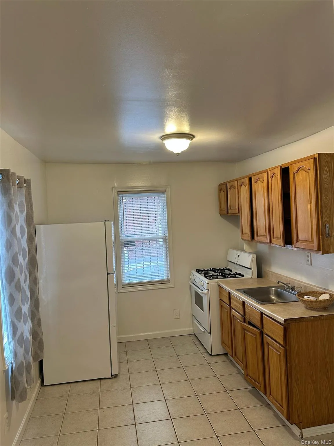 Kitchen with white appliances, brown cabinets, light countertops, and light tile patterned floors Kitchen with white appliances, brown cabinets, light countertops, and light tile patterned floors