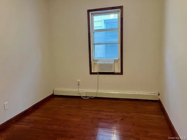 Unfurnished room with dark wood-type flooring, baseboard heating, and cooling unit Unfurnished room with dark wood-type flooring, baseboard heating, and cooling unit