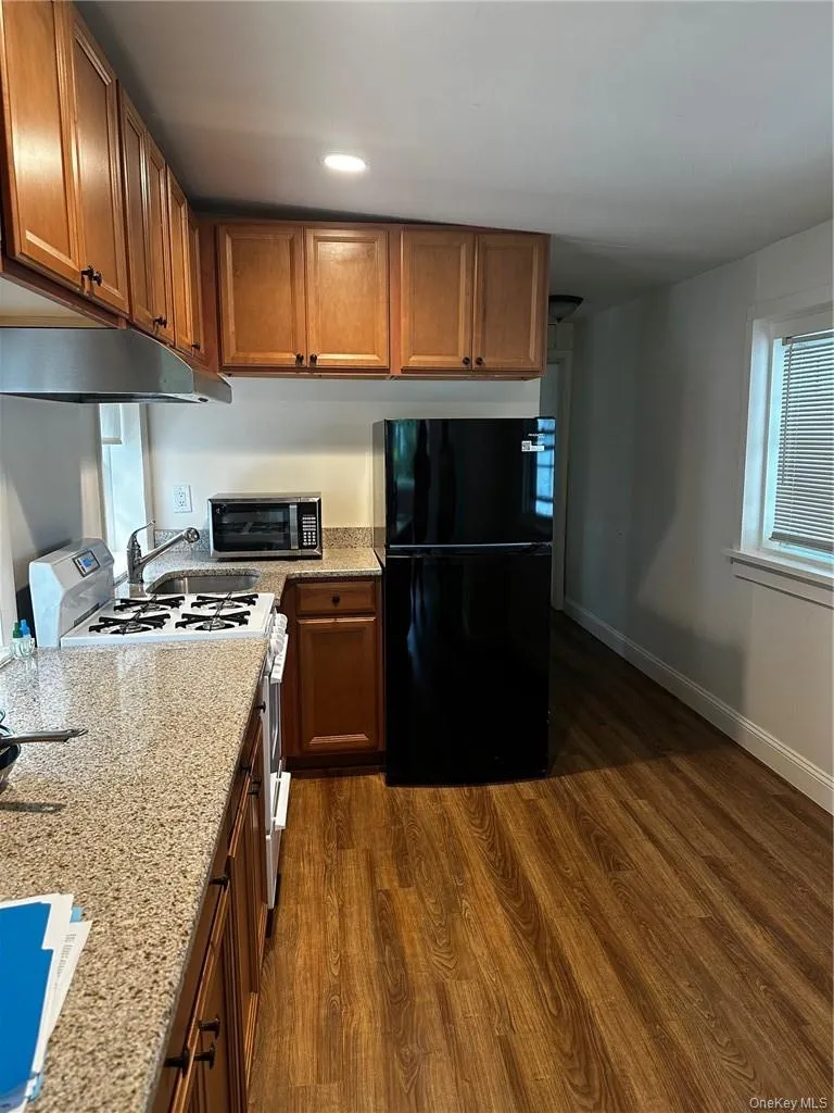 Kitchen with black fridge, range hood, stove, and dark wood-type flooring Kitchen with black fridge, range hood, stove, and dark wood-type flooring