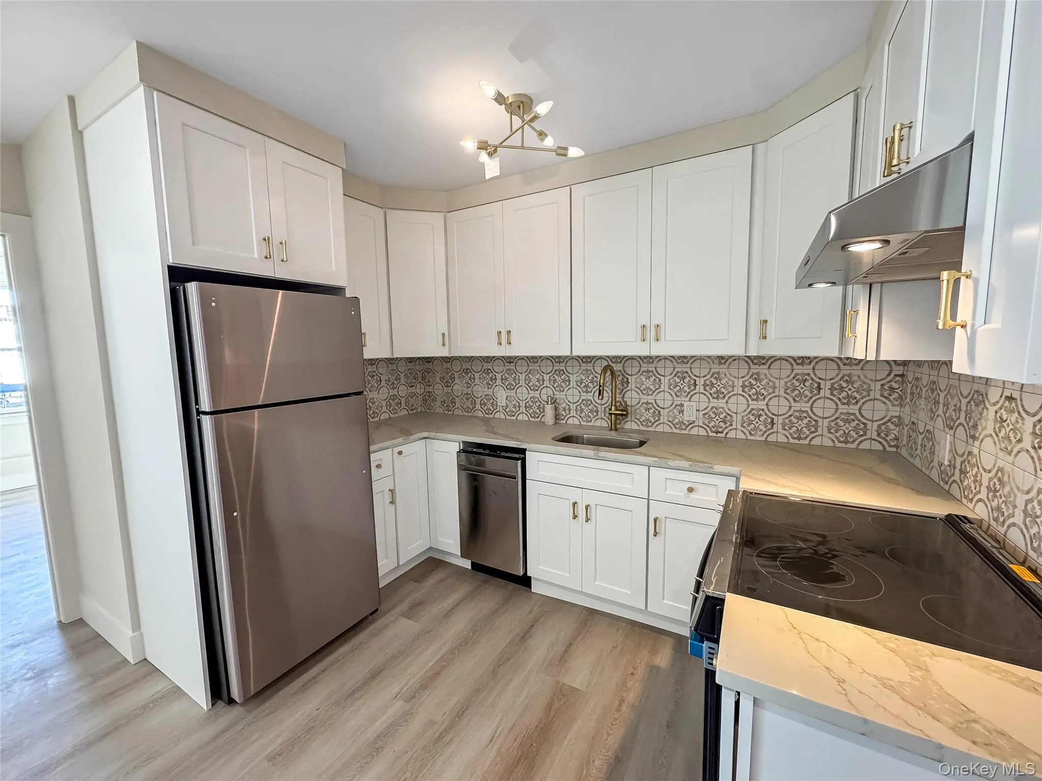Kitchen with light stone counters, stainless steel appliances, white cabinetry, and under cabinet range hood Kitchen with light stone counters, stainless steel appliances, white cabinetry, and under cabinet range hood