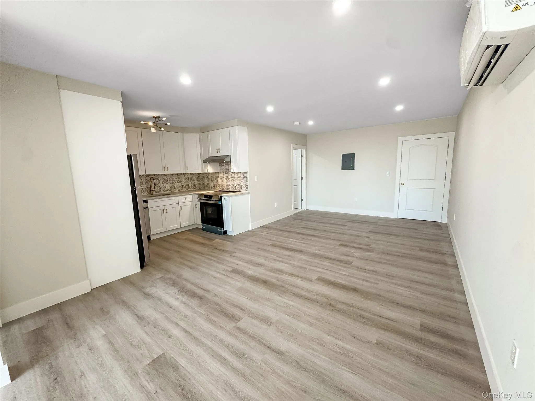 Unfurnished living room featuring a wall unit AC, light wood finished floors, recessed lighting, and electric panel Unfurnished living room featuring a wall unit AC, light wood finished floors, recessed lighting, and electric panel