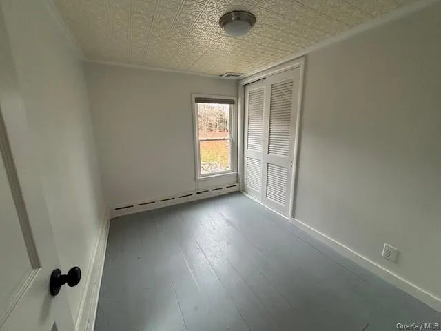 Unfurnished bedroom with an ornate ceiling, a baseboard radiator, hardwood / wood-style floors, a closet, and ornamental molding Unfurnished bedroom with an ornate ceiling, a baseboard radiator, hardwood / wood-style floors, a closet, and ornamental molding