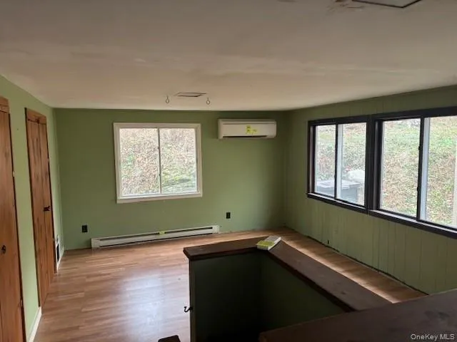 Spare room featuring baseboard heating, plenty of natural light, an AC wall unit, and wood finished floors Spare room featuring baseboard heating, plenty of natural light, an AC wall unit, and wood finished floors