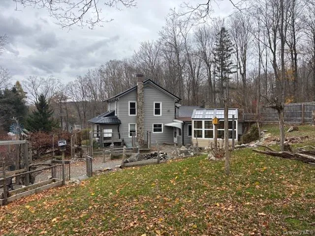 Rear view of property featuring a chimney, view of wooded area, a gate, and a vegetable garden Rear view of property featuring a chimney, view of wooded area, a gate, and a vegetable garden