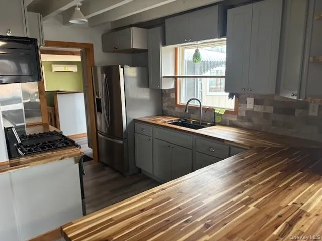Kitchen featuring butcher block counters, stainless steel refrigerator with ice dispenser, gray cabinetry, decorative backsplash, and black microwave Kitchen featuring butcher block counters, stainless steel refrigerator with ice dispenser, gray cabinetry, decorative backsplash, and black microwave