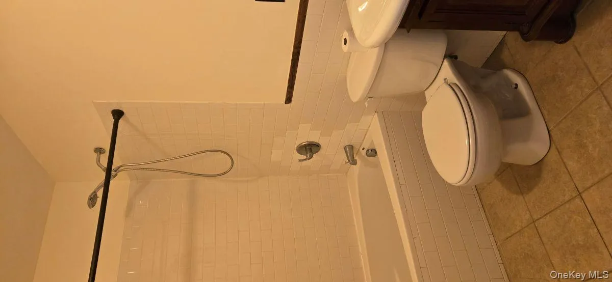 Full bath featuring vanity, tile walls, a wainscoted wall, shower / tub combination, and light tile patterned floors Full bath featuring vanity, tile walls, a wainscoted wall, shower / tub combination, and light tile patterned floors