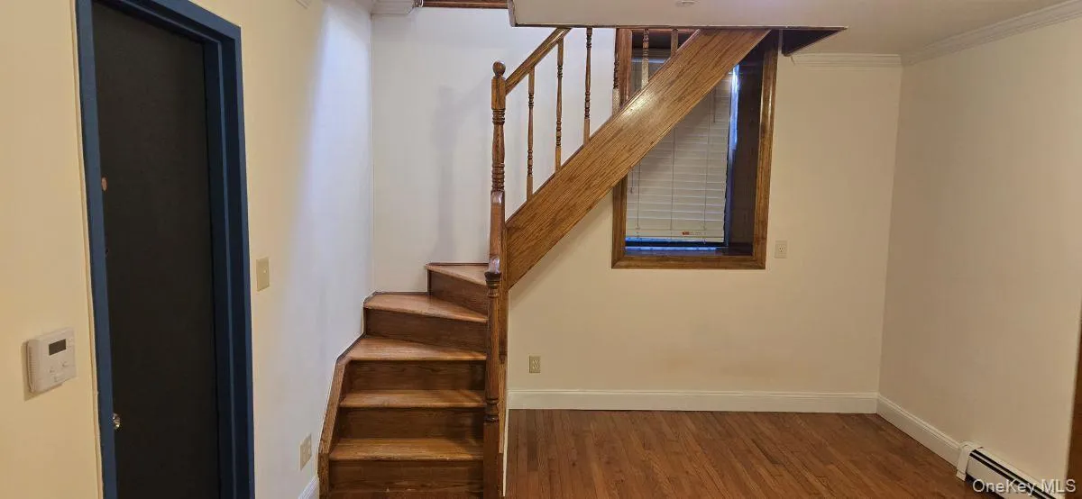 Stairway featuring crown molding, baseboard heating, and wood finished floors Stairway featuring crown molding, baseboard heating, and wood finished floors